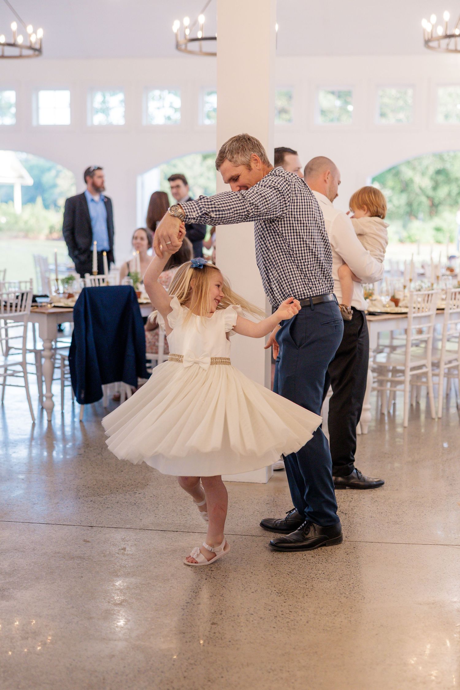 Wedding reception guests dancing in pairs across a bright white venue space with elegant decor.
