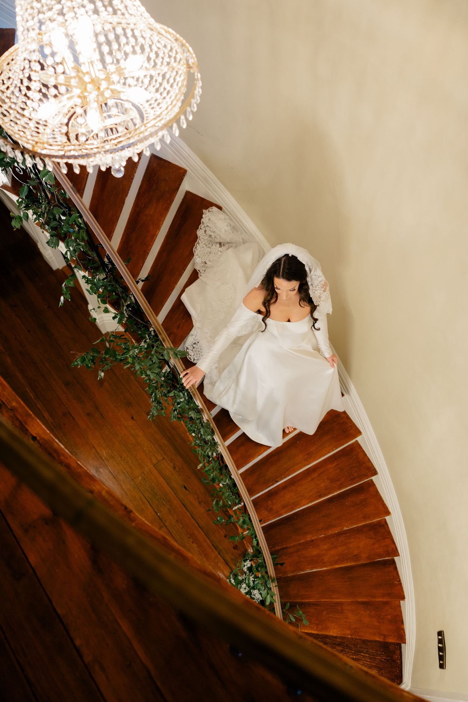 White wedding dress cascading down a curved staircase decorated with greenery and wooden steps.