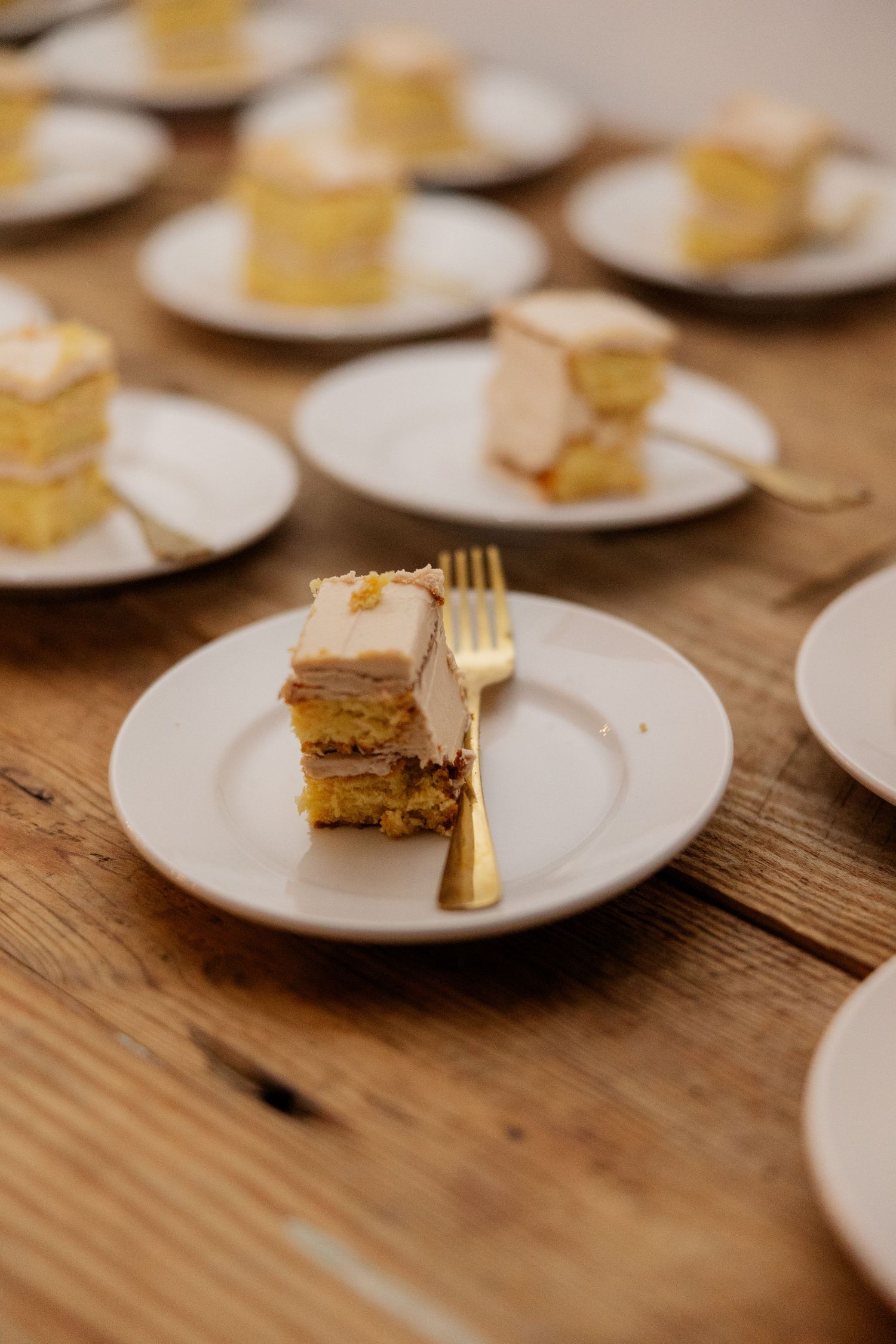 White plates with partially eaten slices of yellow cake line a rustic wooden table at an event.