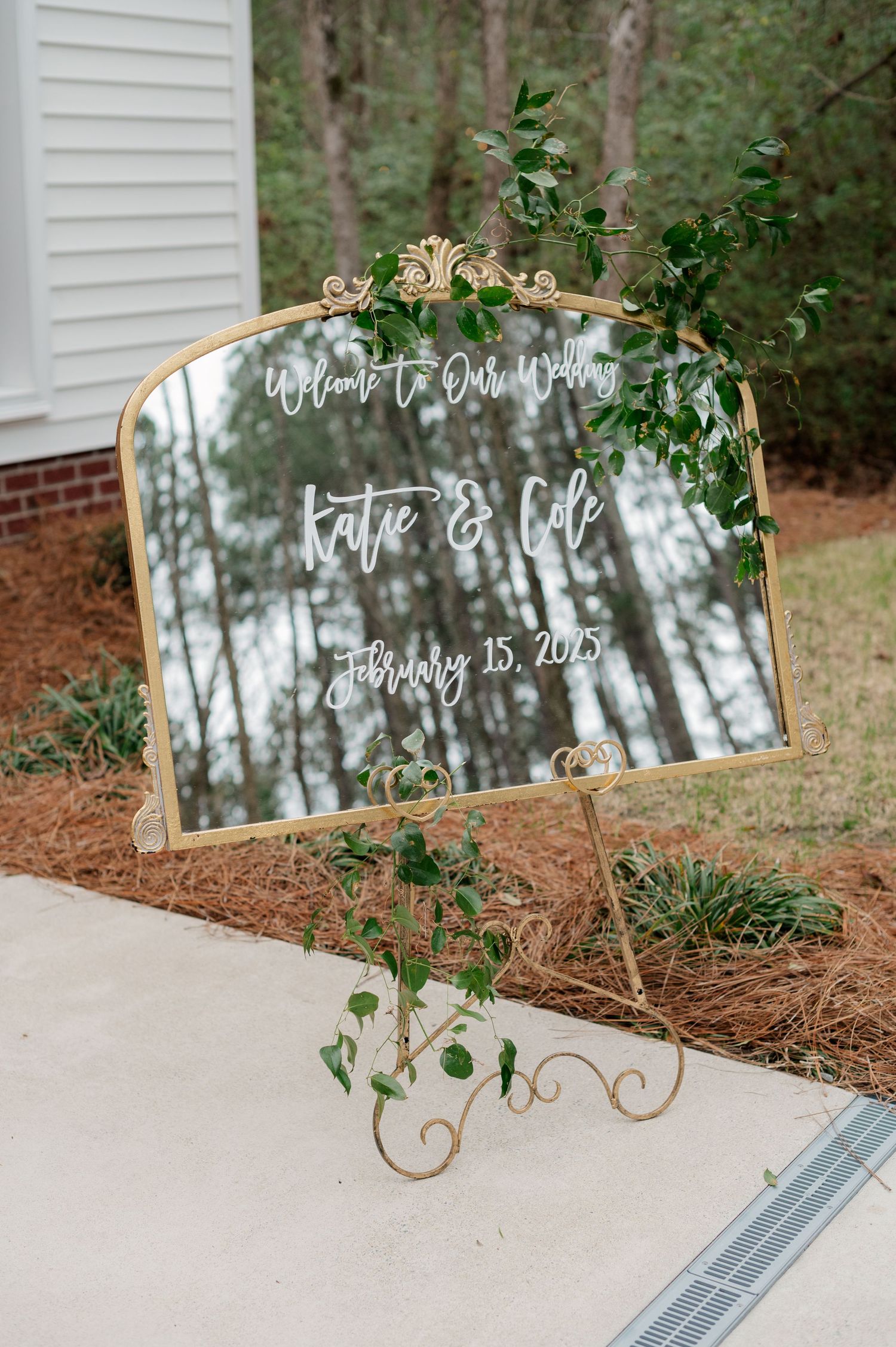 A decorative mirror wedding welcome sign with greenery and golden accents.