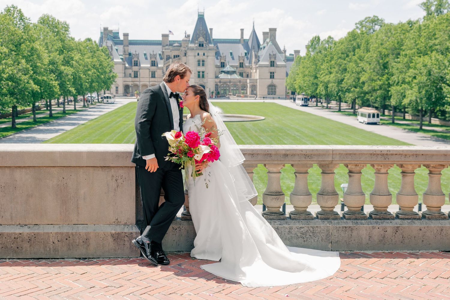 Bride and groom share a romantic kiss at Biltmore Estate, with lush gardens and the grand chateau in the background.