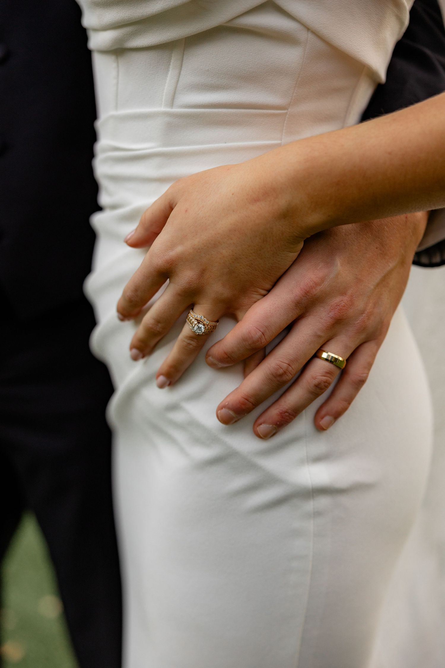 Close-up of newlyweds' hands showing their wedding rings against a white wedding dress.