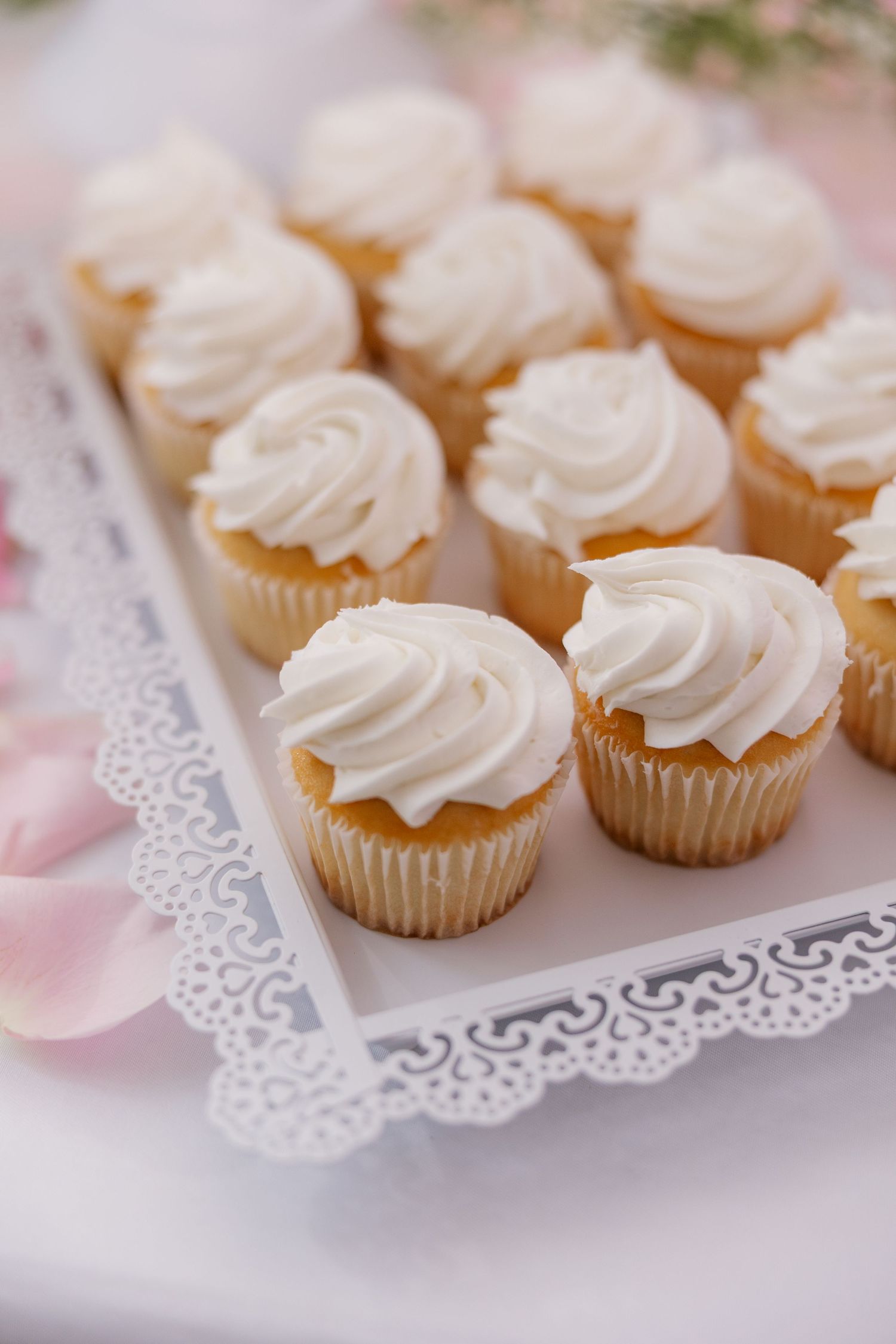 Mini vanilla cupcakes with white frosting arranged on a delicate lace doily.
