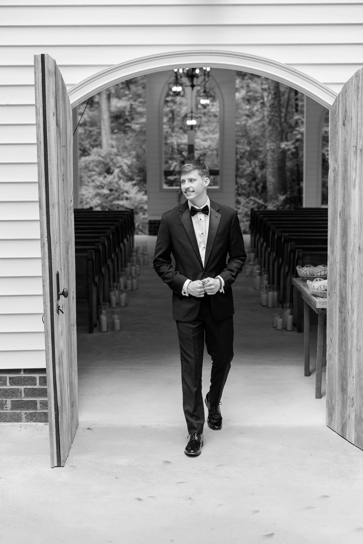 Classic black tuxedo wedding photo taken inside a charming white chapel with wooden pews.