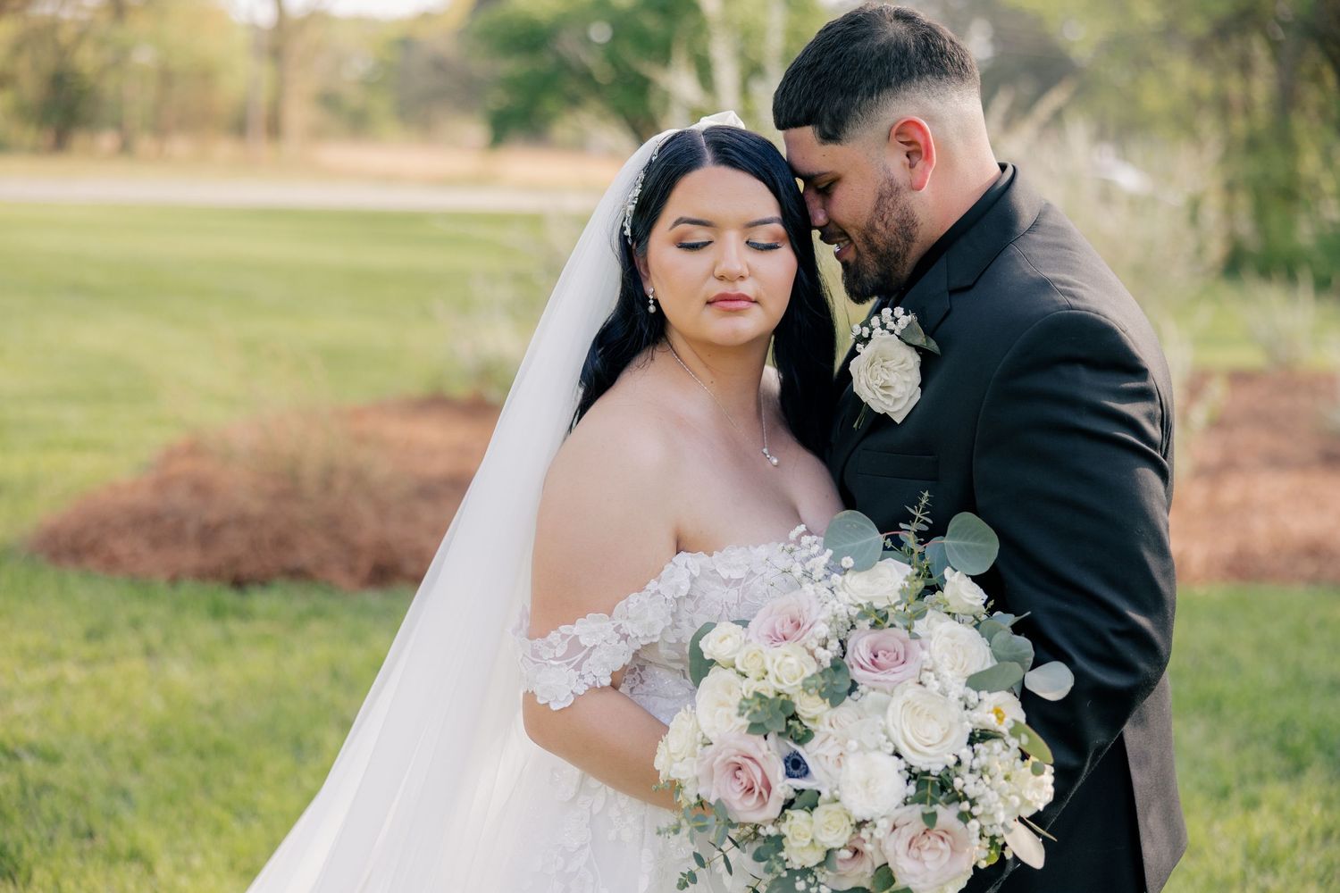 A romantic wedding couple shares tender moments in an outdoor setting with blush and cream floral bouquets and arrangements.