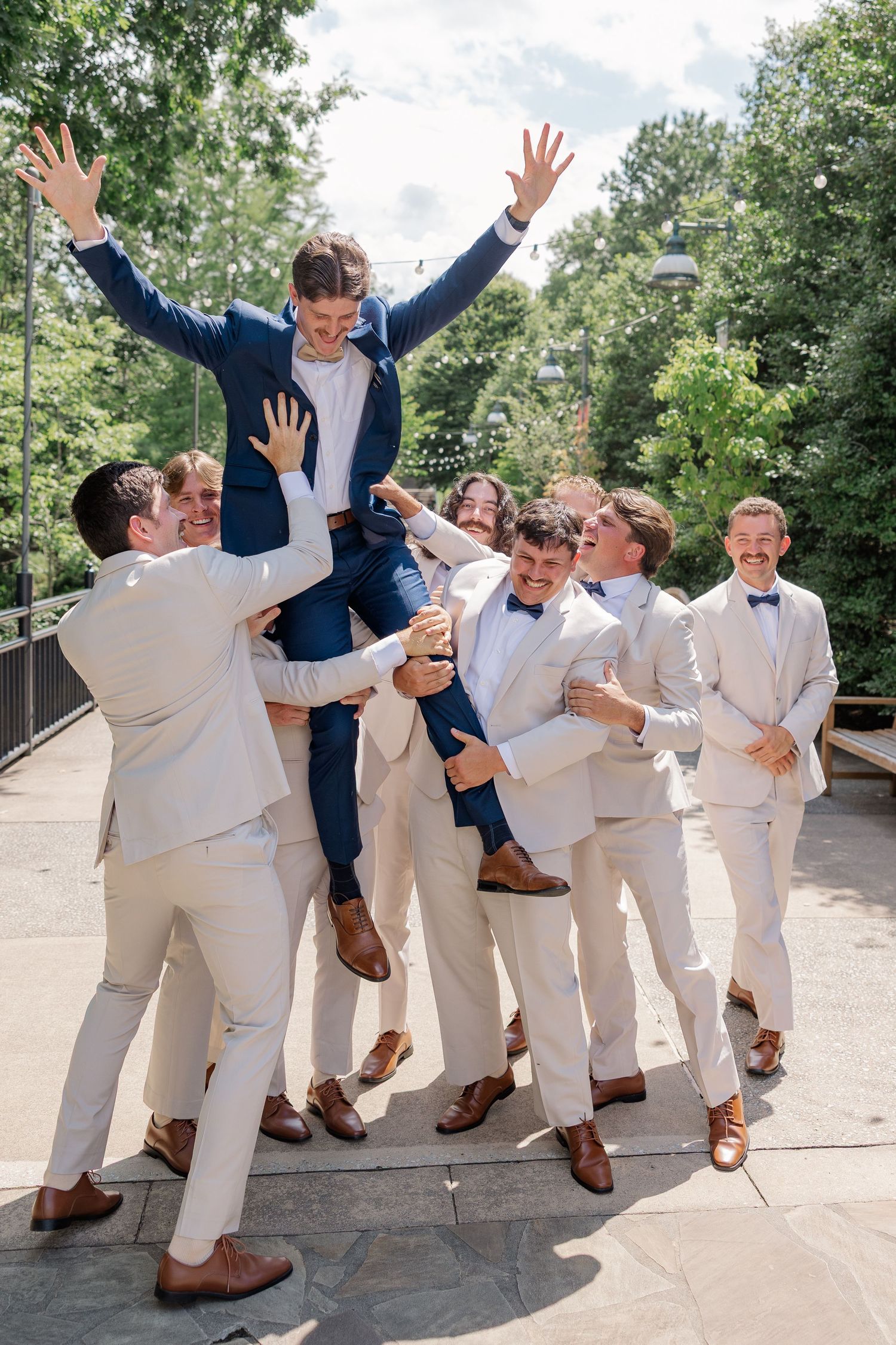 Groomsmen in white suits and bowties perform a fun jumping pose together outdoors.