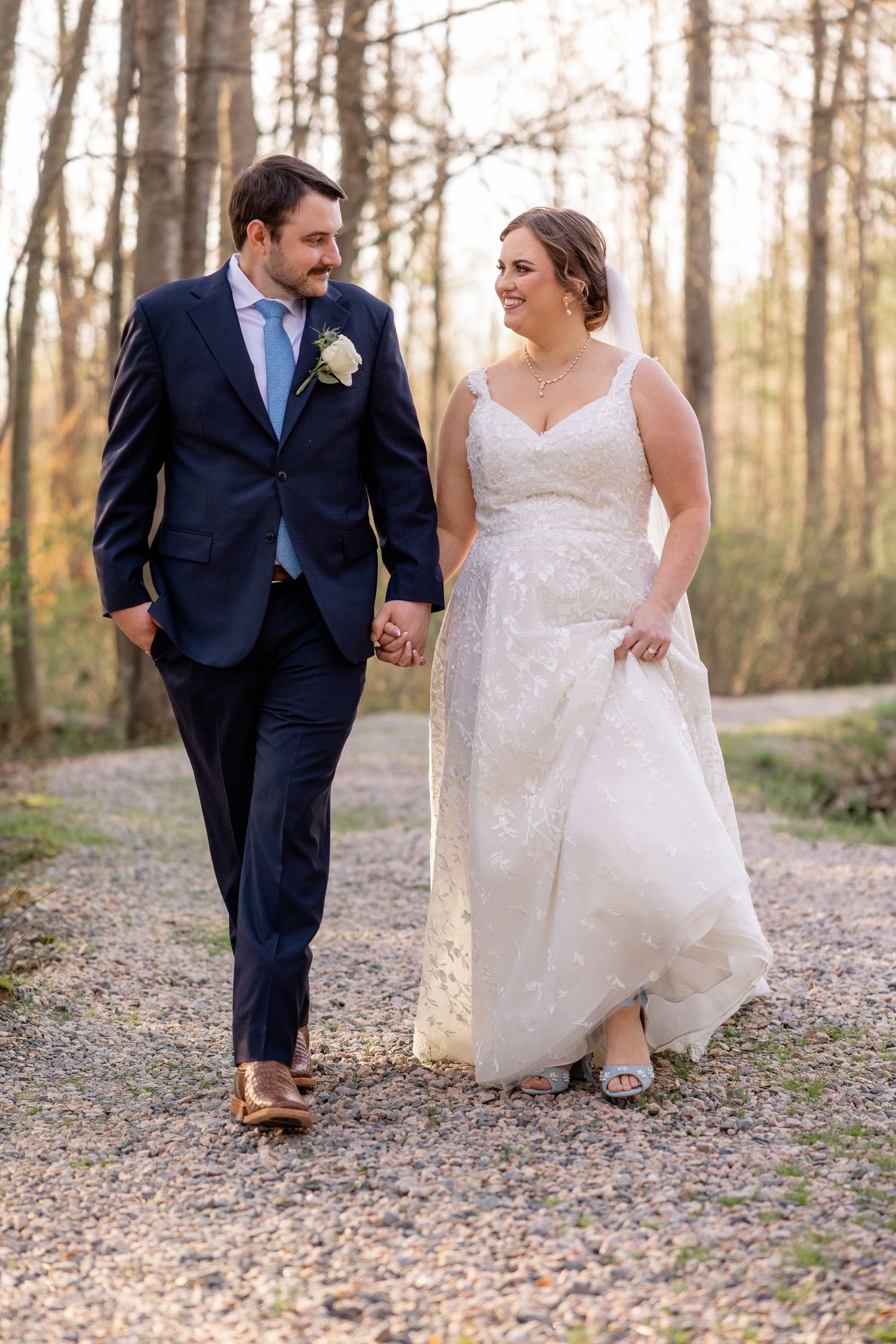 Couple walking along a woodland path, with the bride wearing a white dress and groom in navy suit.