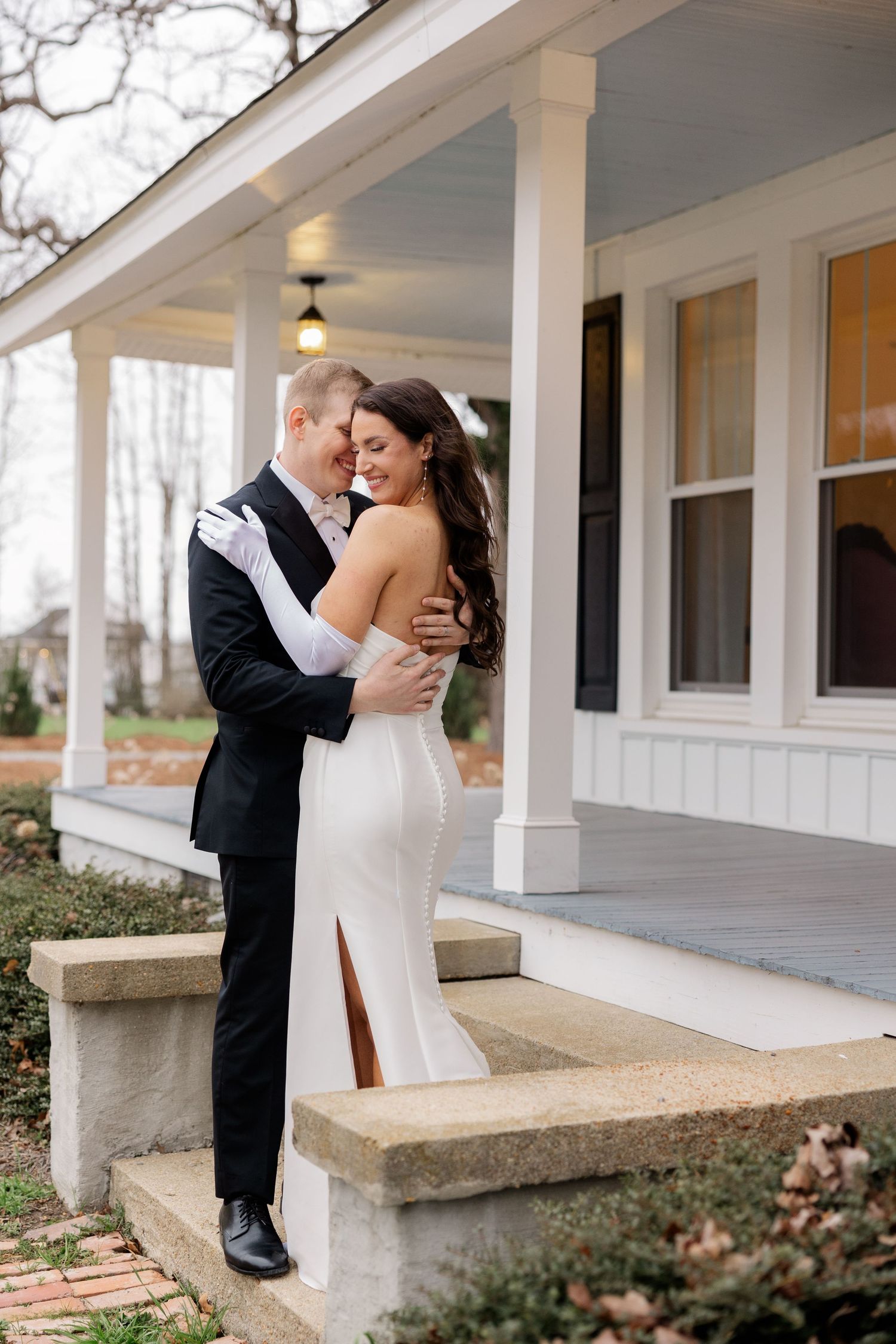 Newlyweds share an intimate moment on a white columned porch during their wedding day.