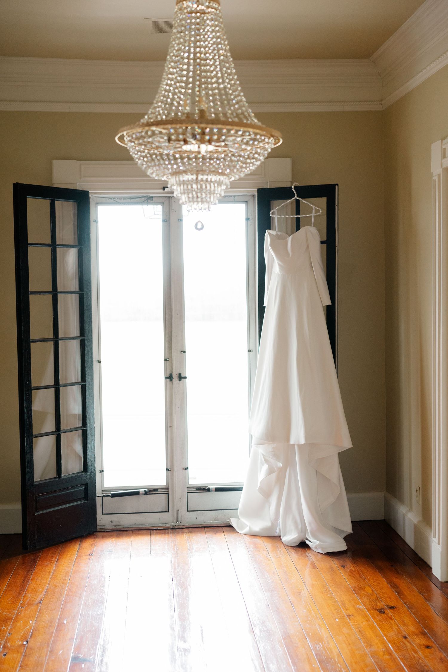 Elegant white wedding dress on display in a room with polished hardwood floors and crystal chandeliers.