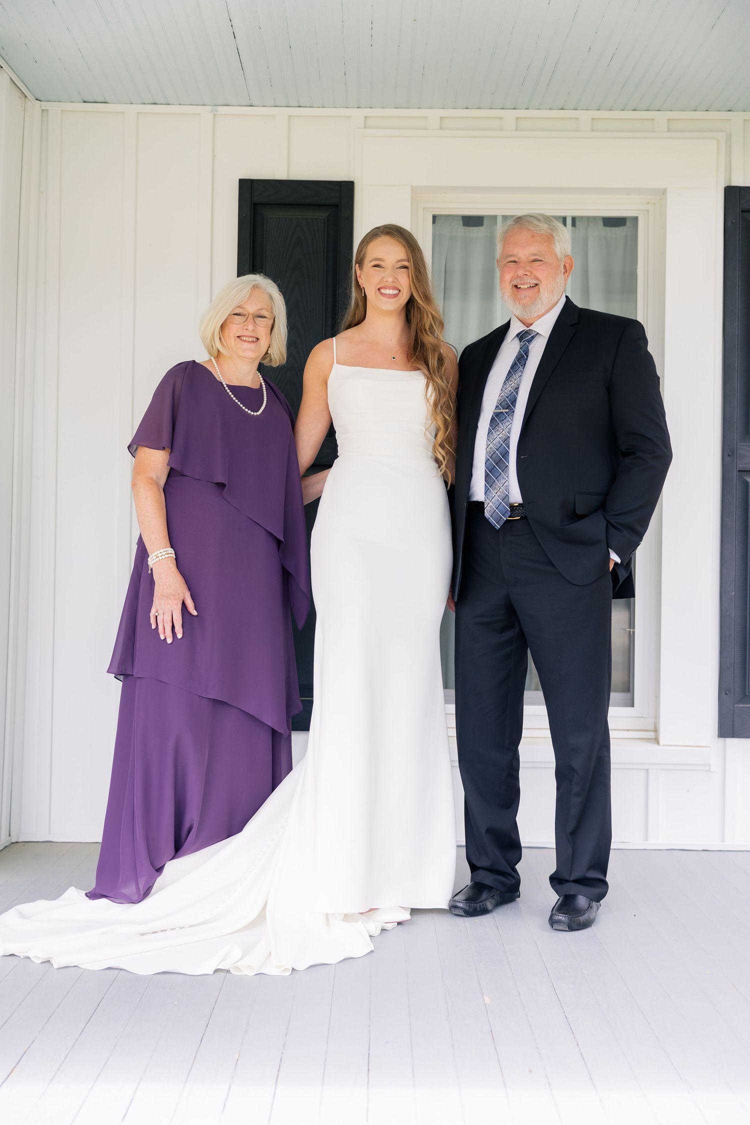 Wedding party poses on a white porch with the bride in white and guest in purple dresses.