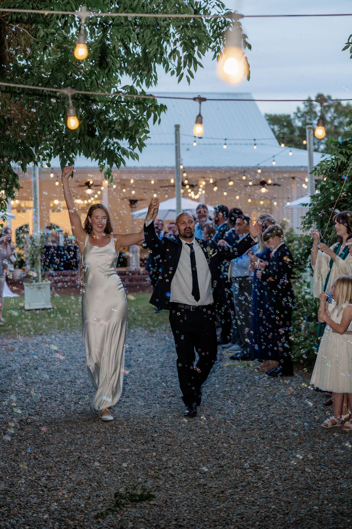 Joyful wedding exit with guests throwing confetti as couple celebrates under string lights.