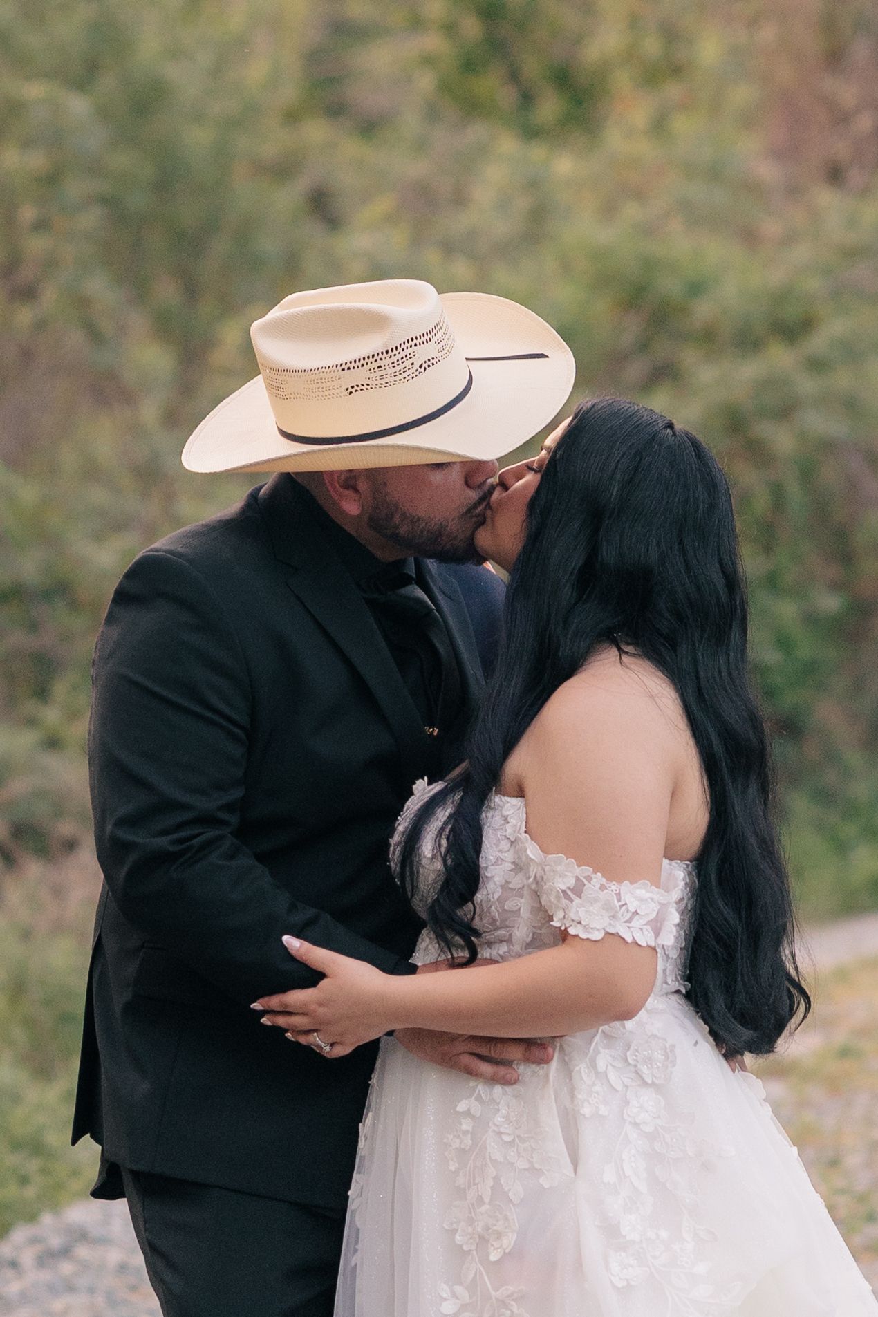 A couple shares first look wedding photos in a rustic outdoor setting with cowboy hat details.