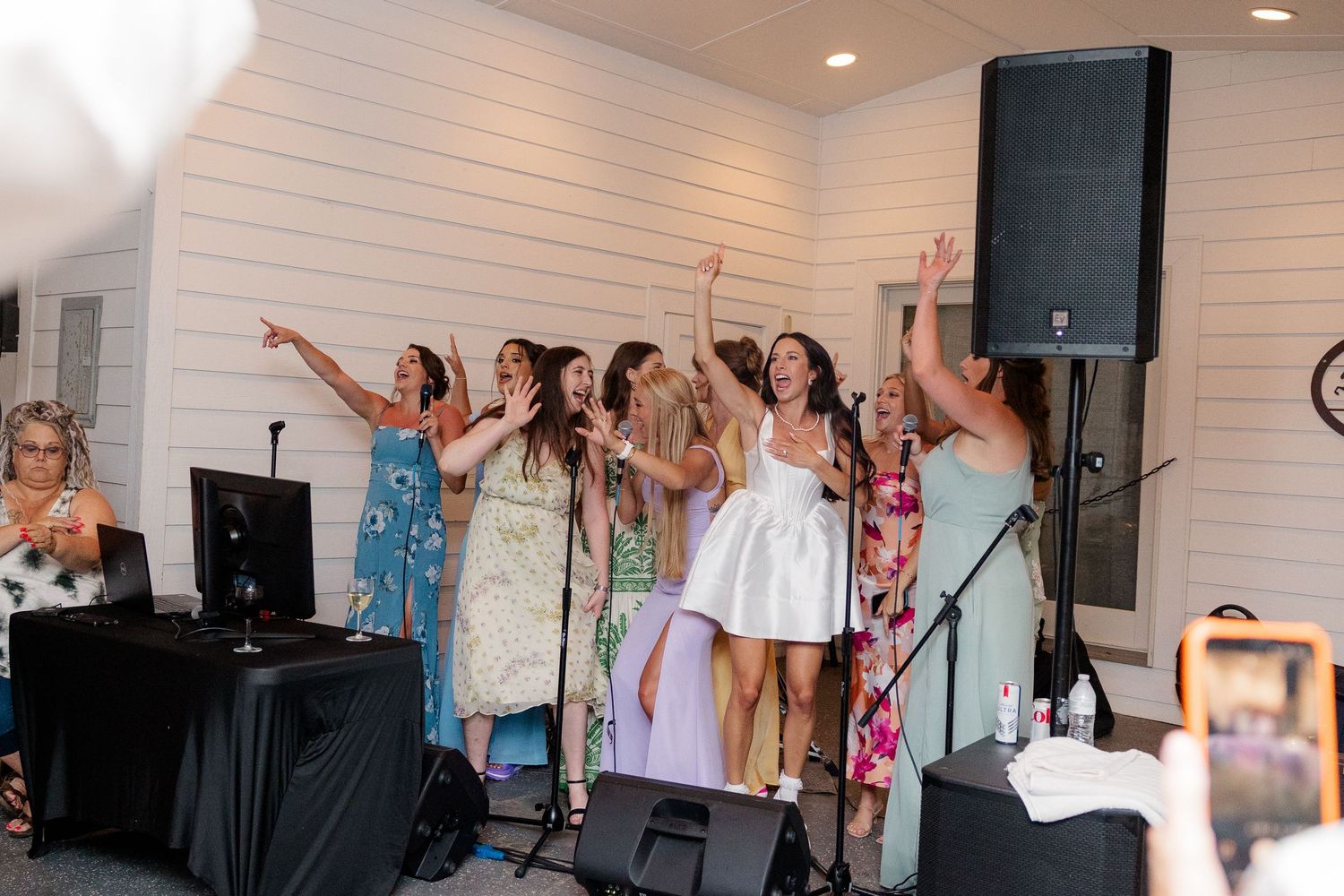 Wedding guests celebrate on a dance floor with raised arms during an indoor reception party.
