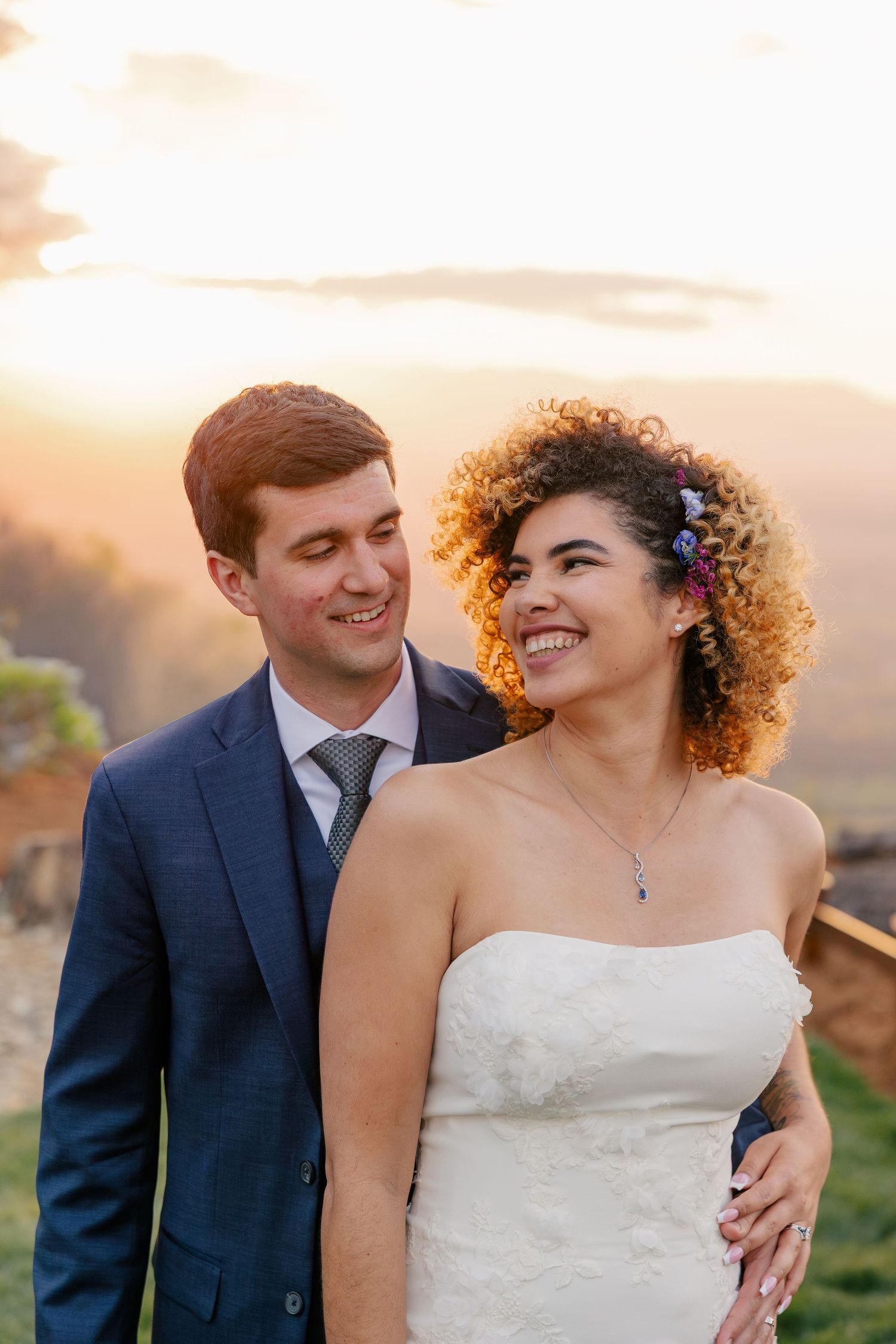 Bride and groom smiling together at golden hour with mountain views in the background at their wedding.
