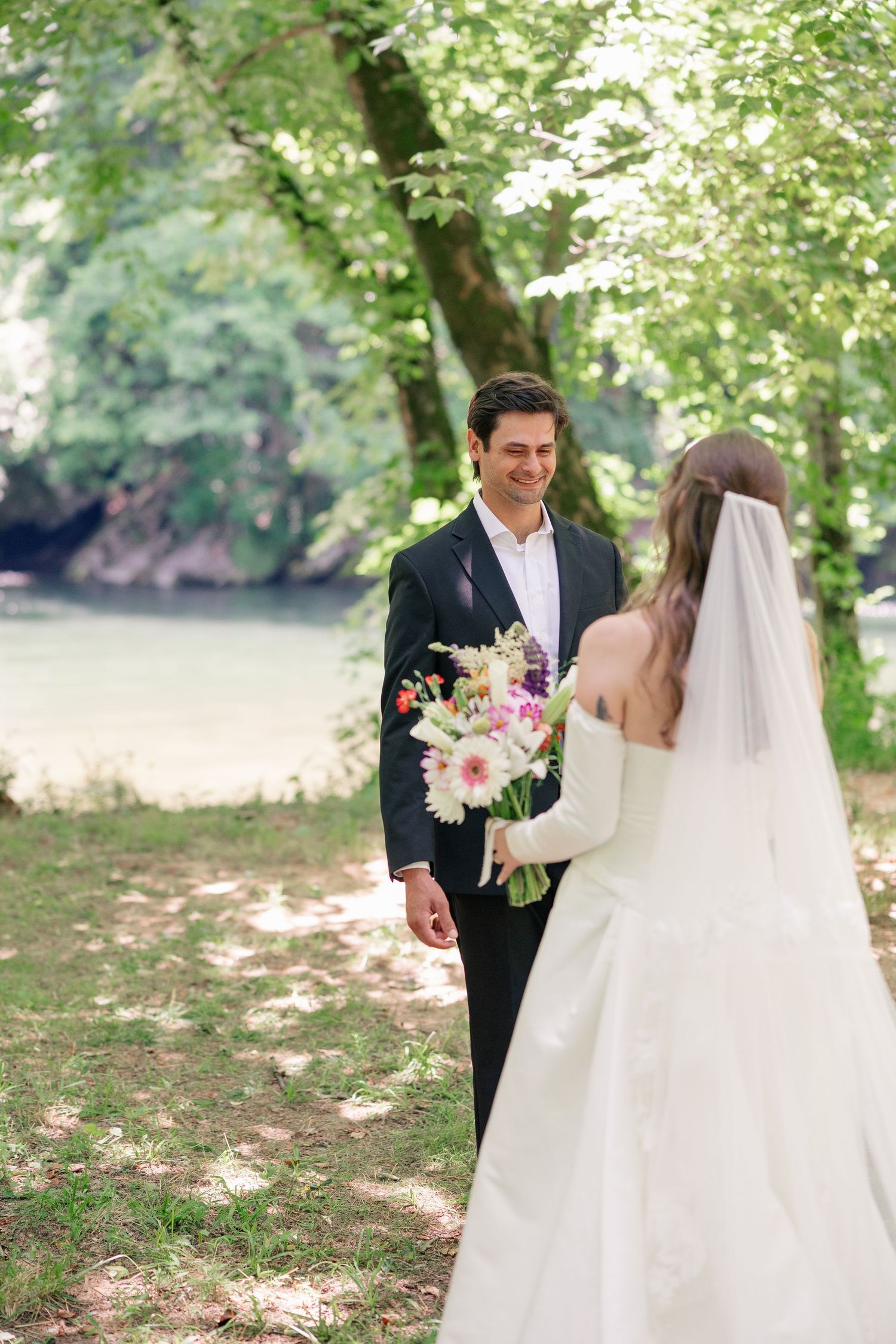 Groom smiles warmly at bride holding a pastel floral bouquet during a romantic outdoor first look.