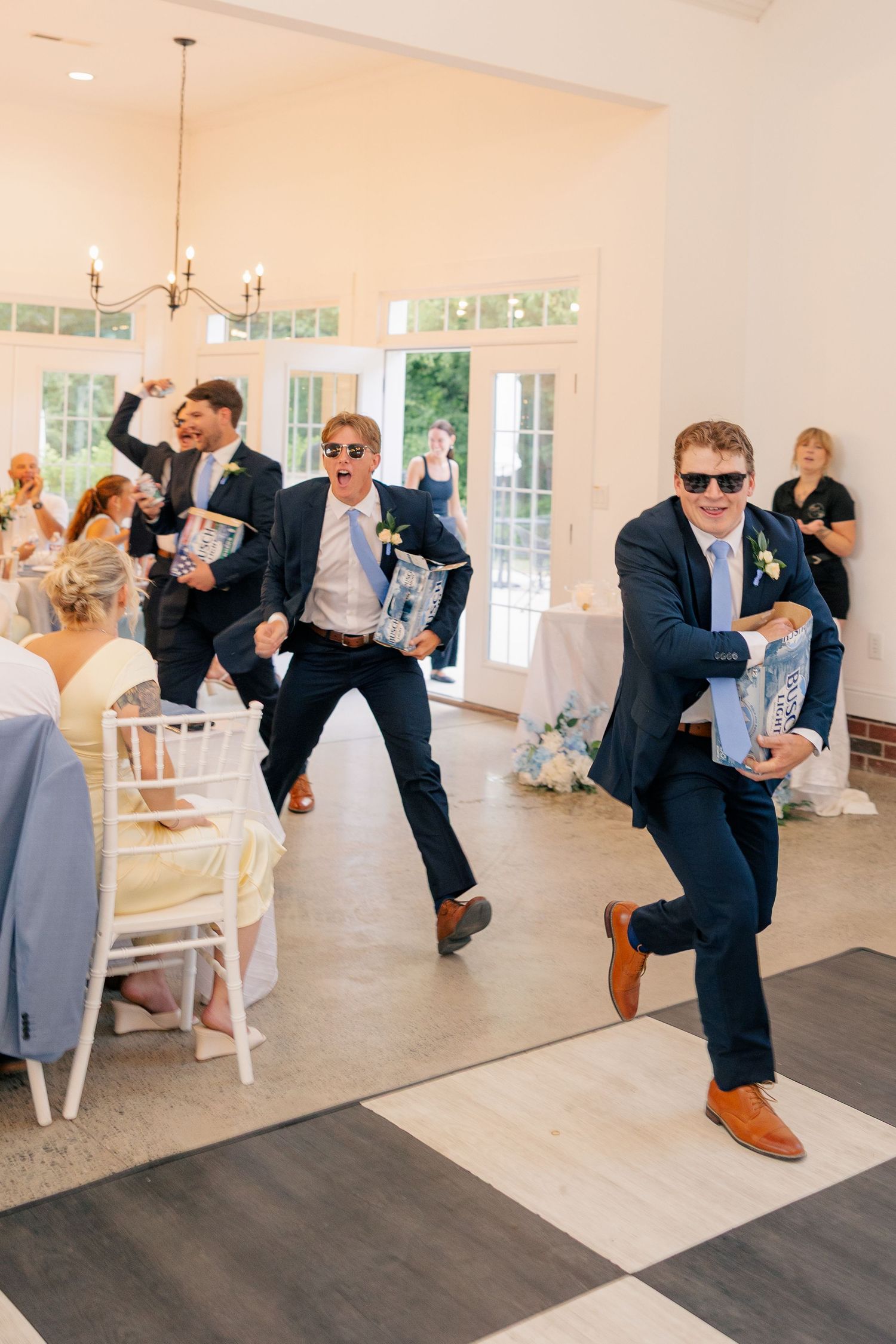 Groomsmen in navy suits and sunglasses make a fun energetic entrance at wedding reception.