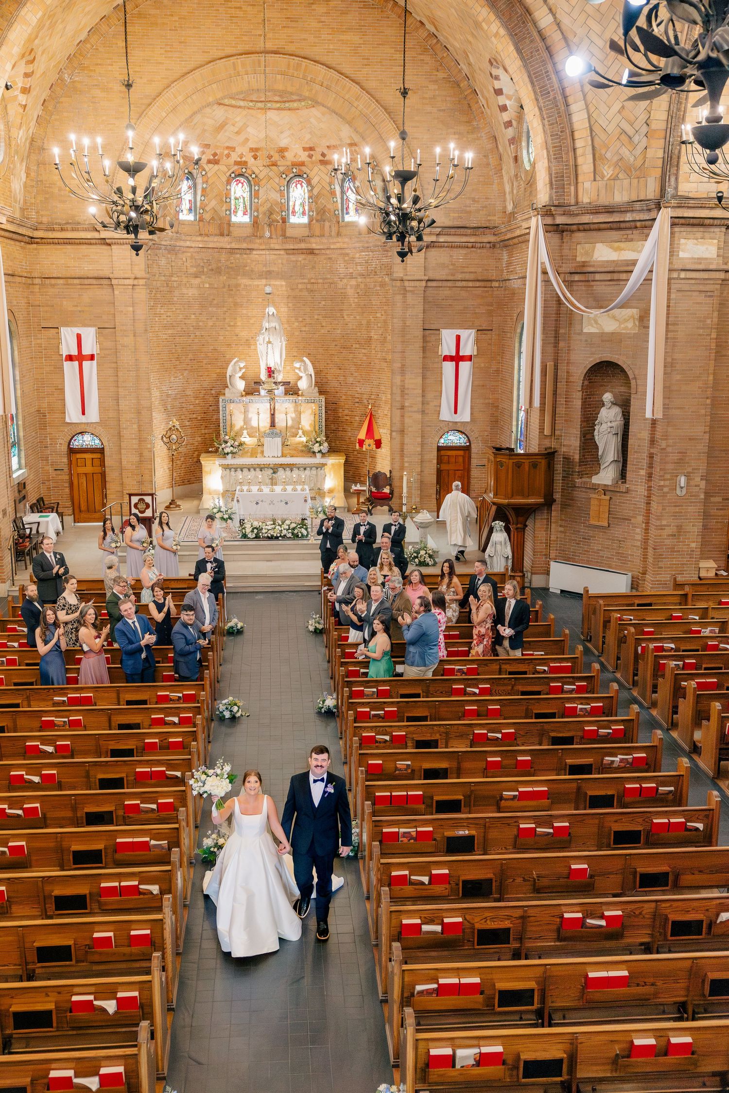 Bride and groom walk down aisle of ornate brick church as guests celebrate their marriage ceremony.