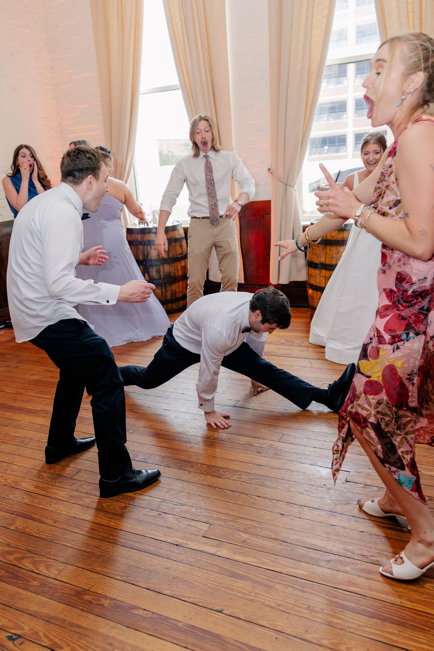 Wedding guests doing energetic dance moves on wooden floor at reception.