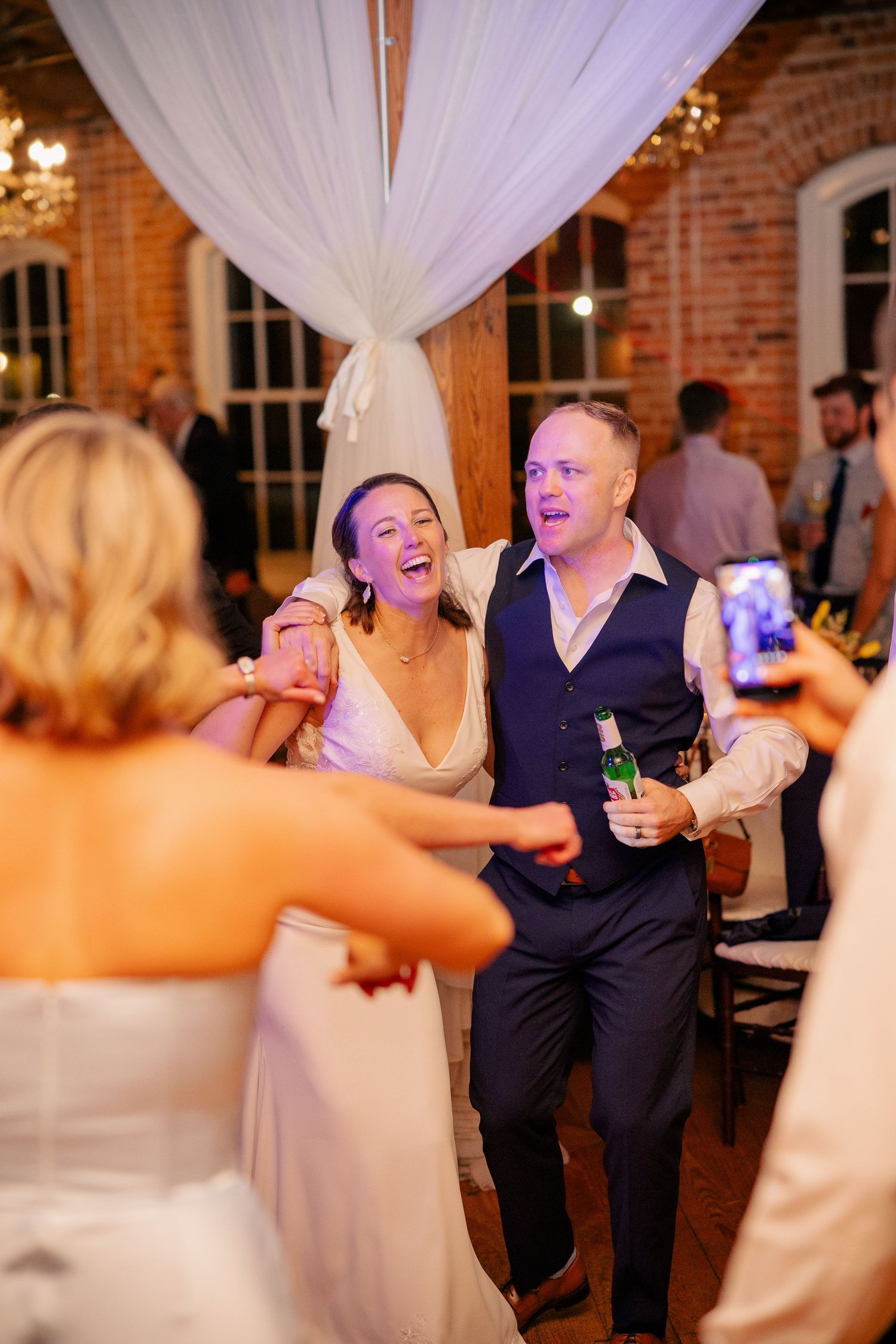 Laughing bride and groom celebrate with guests on the dance floor during wedding reception.