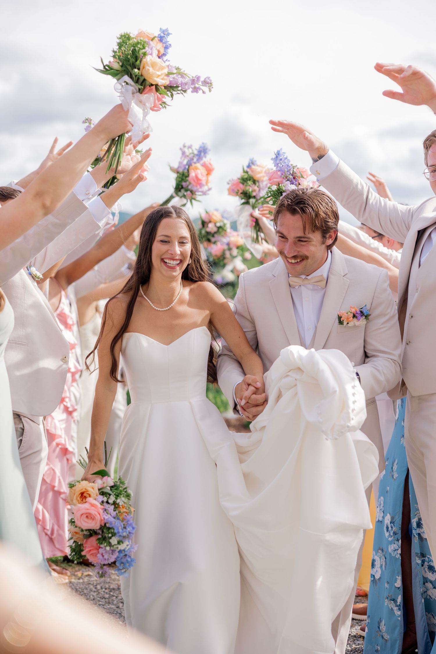 Wedding party celebrating with joyful dance moves in white attire against mountain scenery.