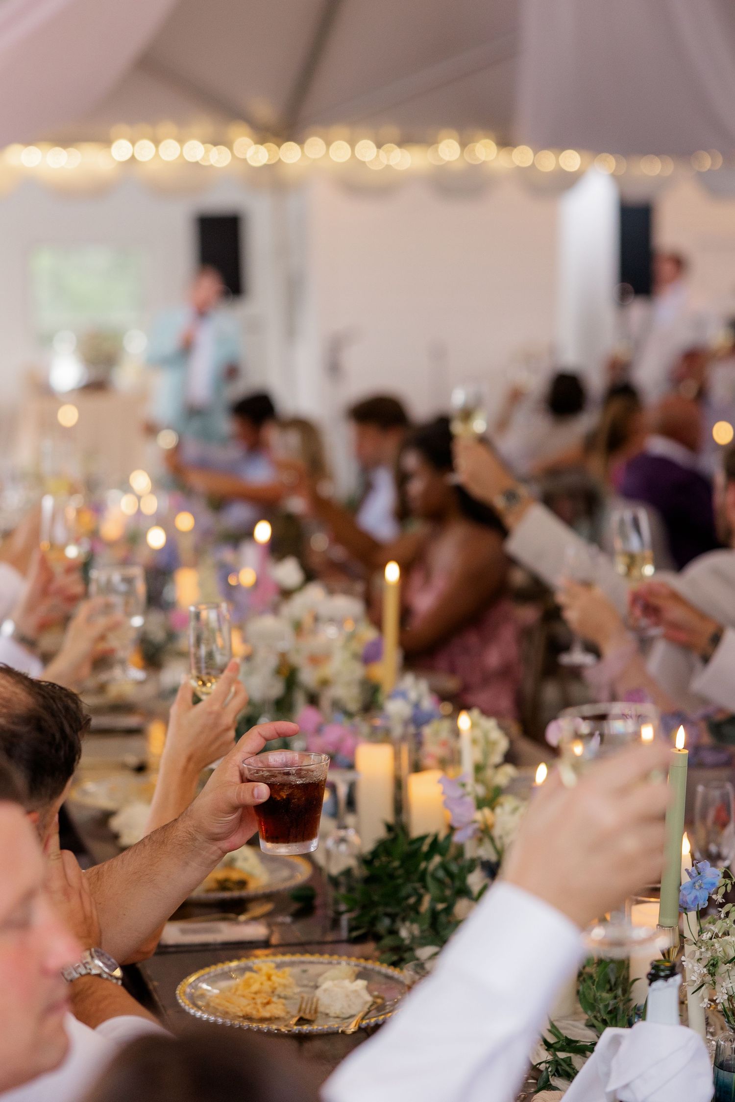 Wedding reception table settings under tent with string lights and candle centerpieces.