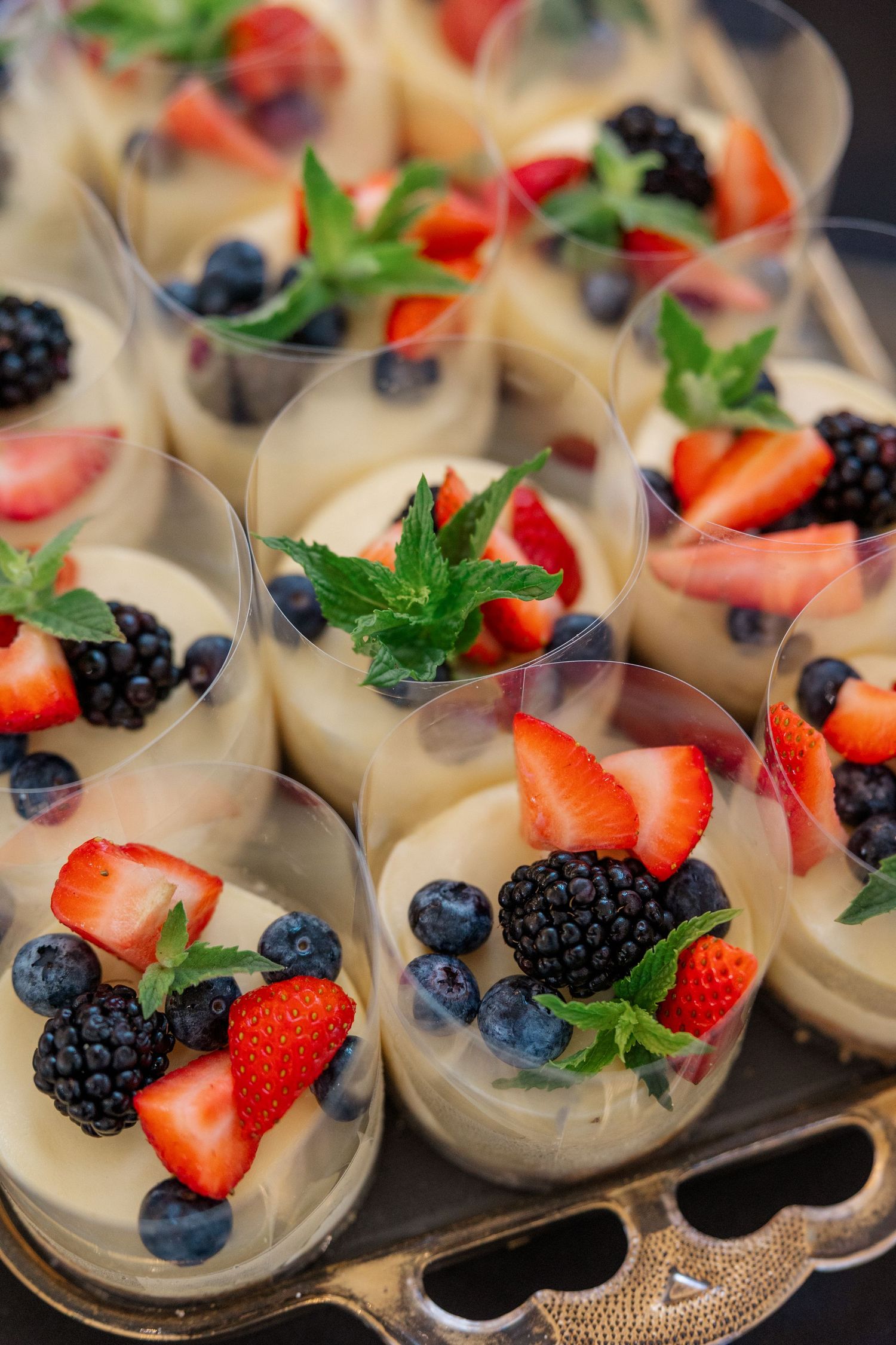 Individual dessert cups filled with creamy mousse topped with fresh berries and mint garnish.