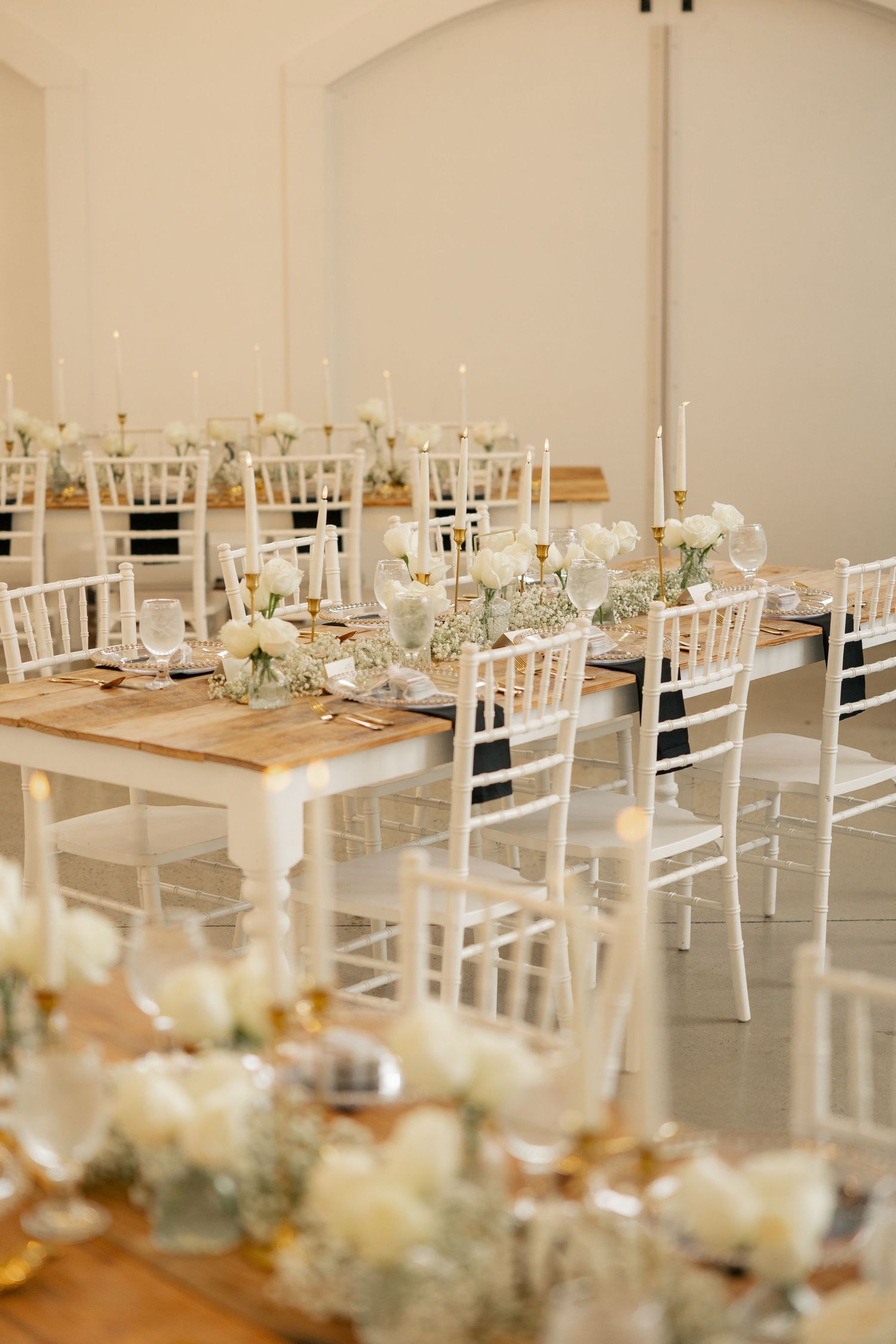 An elegant white and natural wood wedding reception setup with chiavari chairs and table settings.