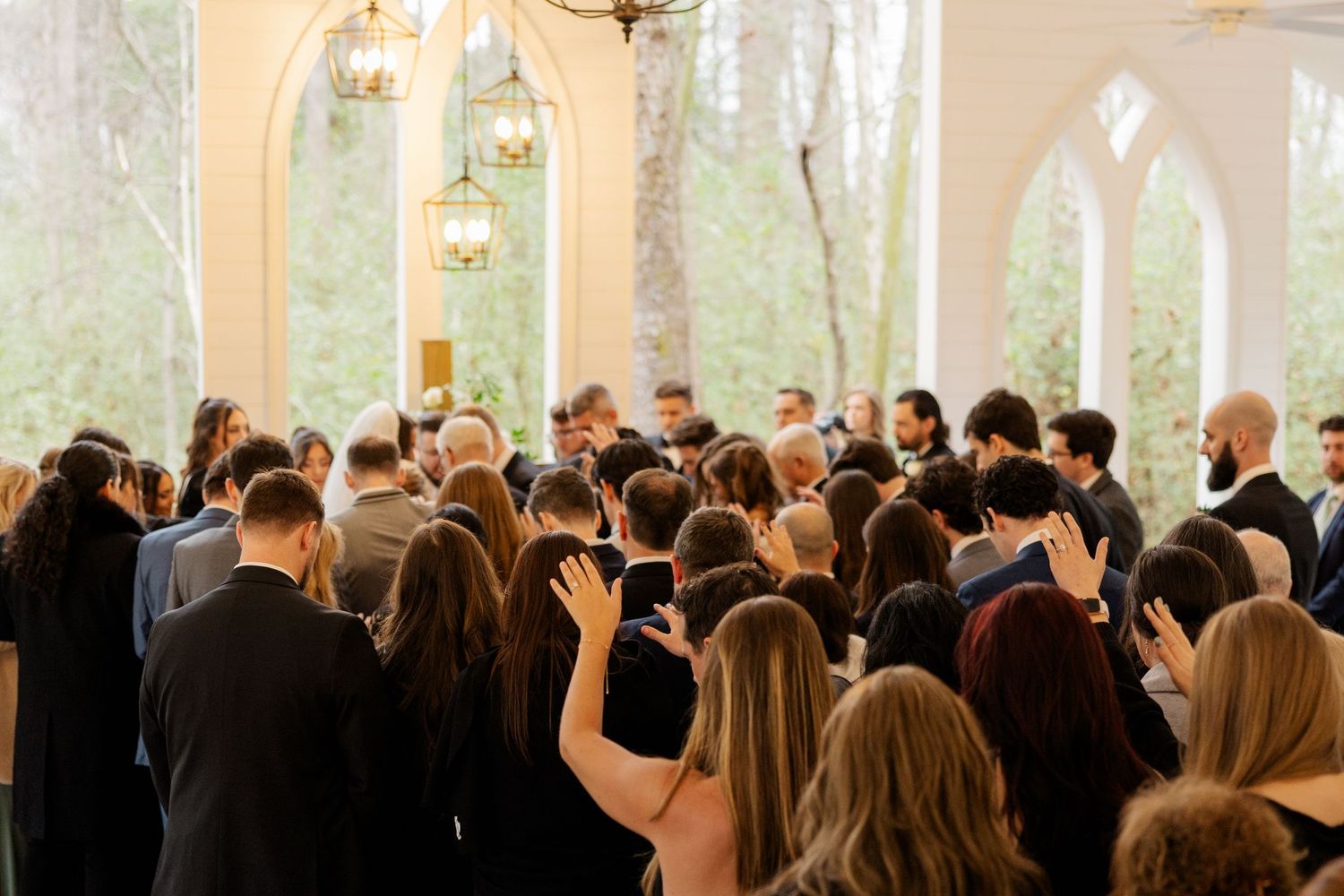 Wedding ceremony guests fill a bright chapel with large arched windows.