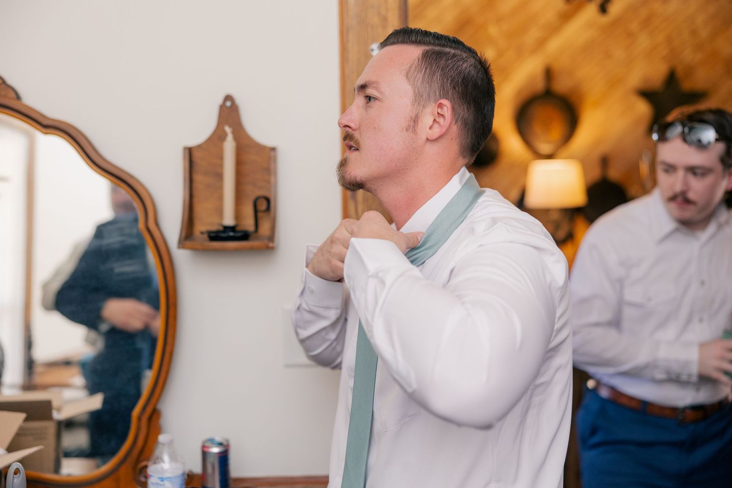 Groomsmen in white dress shirts gather in rustic indoor setting during wedding preparations.