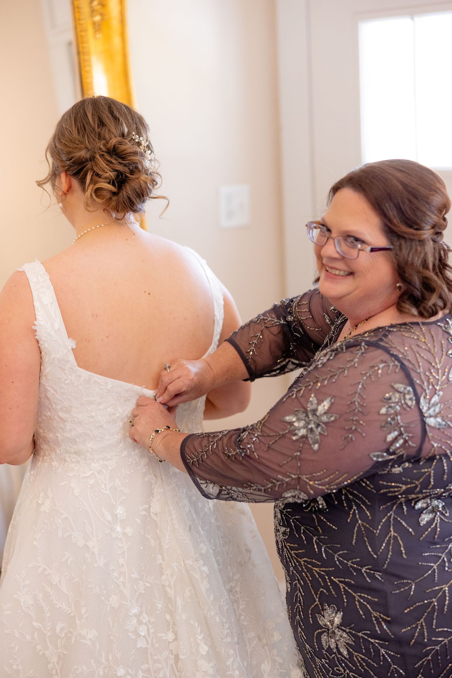 Helper assisting with the back of an elegant white wedding gown during bridal preparations.