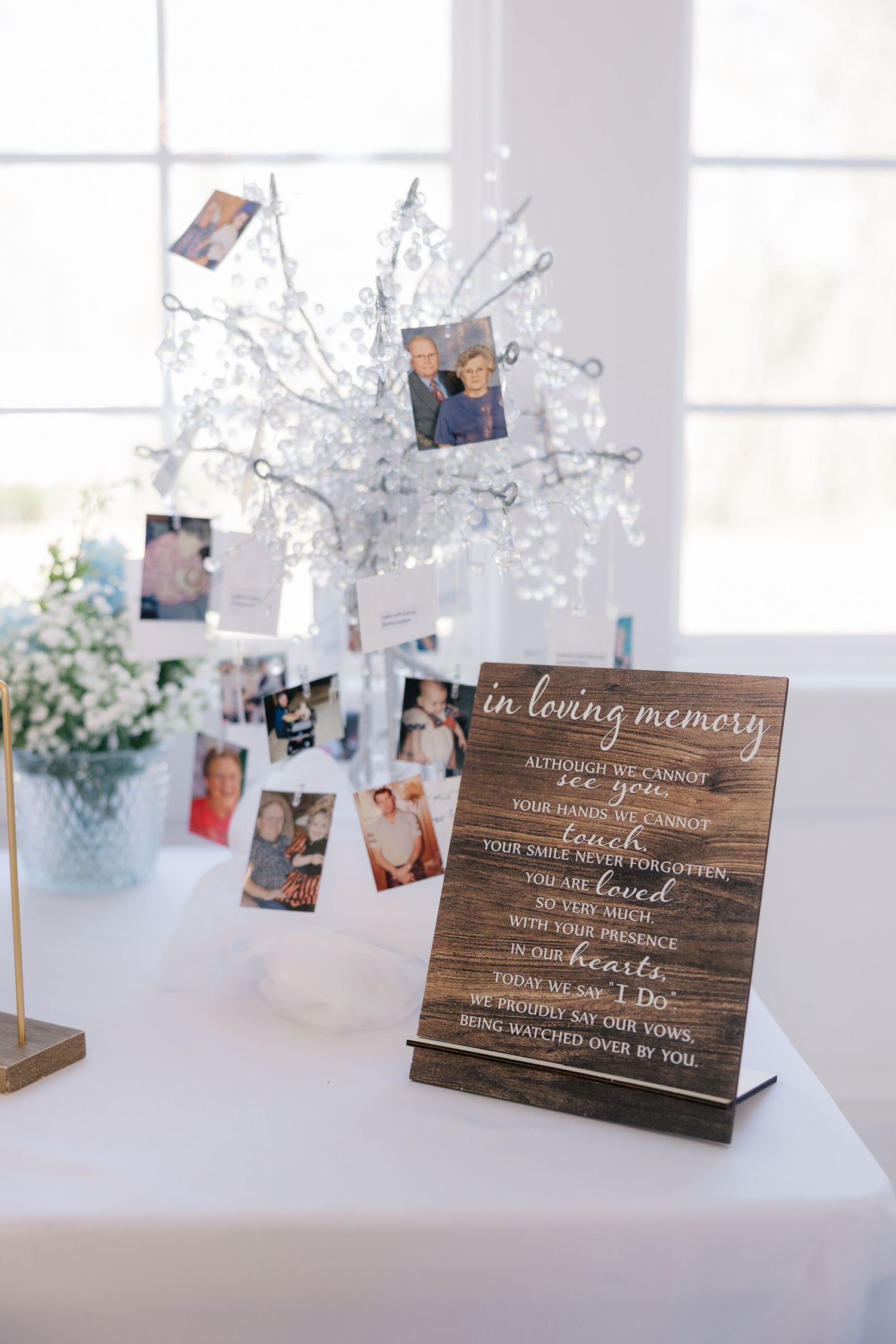 Wooden memorial signs with photos displayed on white tables at wedding reception.