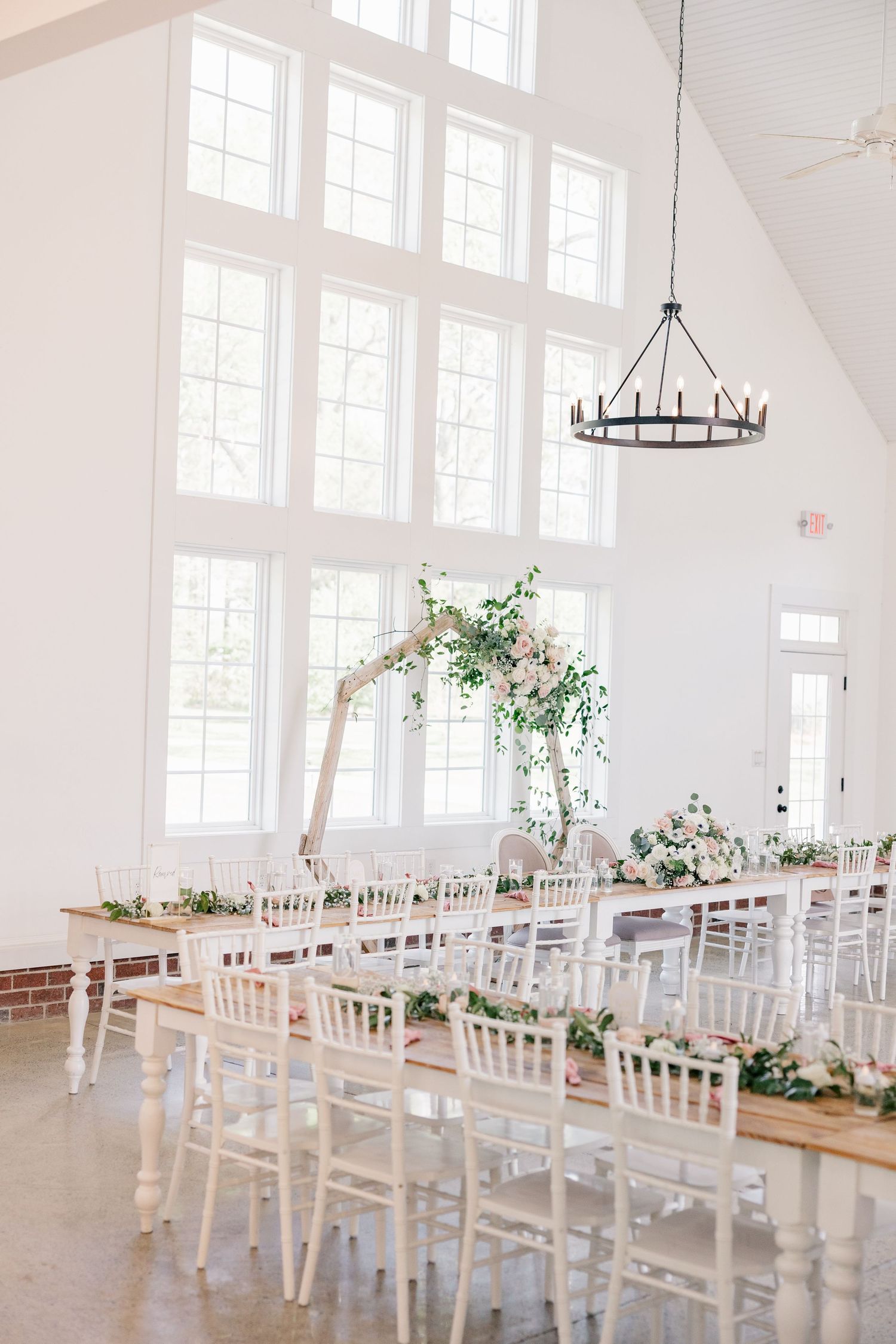 Elegant white reception hall with chiavari chairs and greenery decorations along tables.