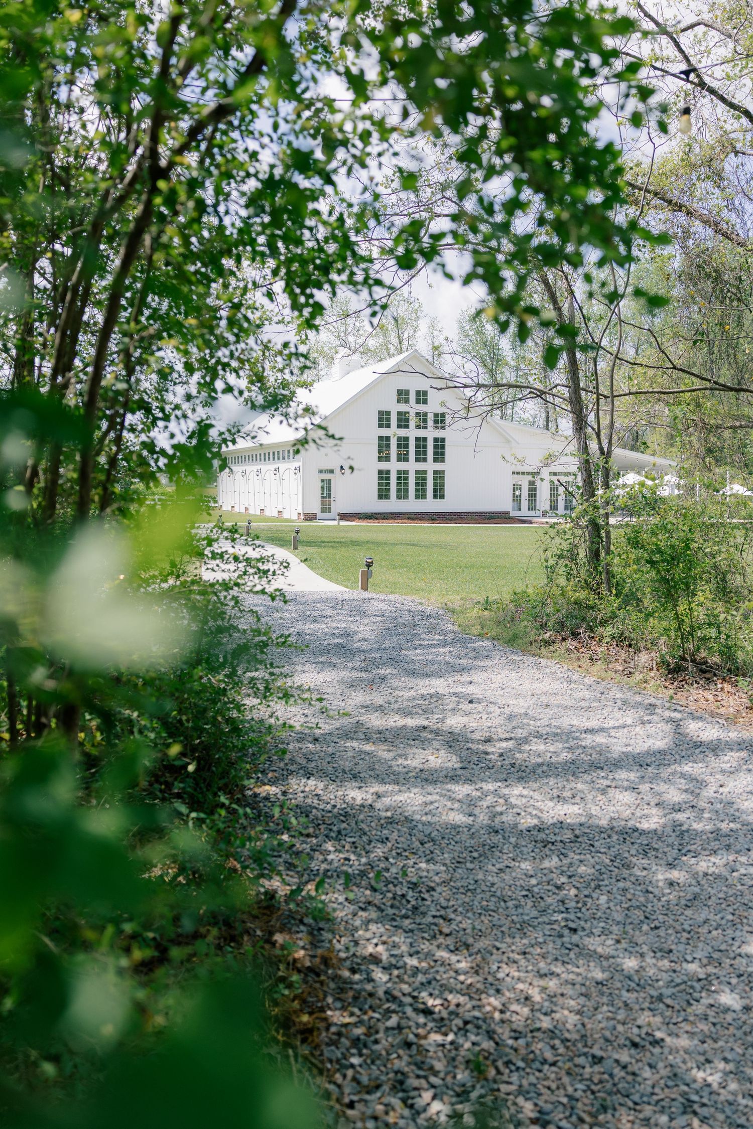 White building visible through winding gravel path with lush green trees framing the serene scene.