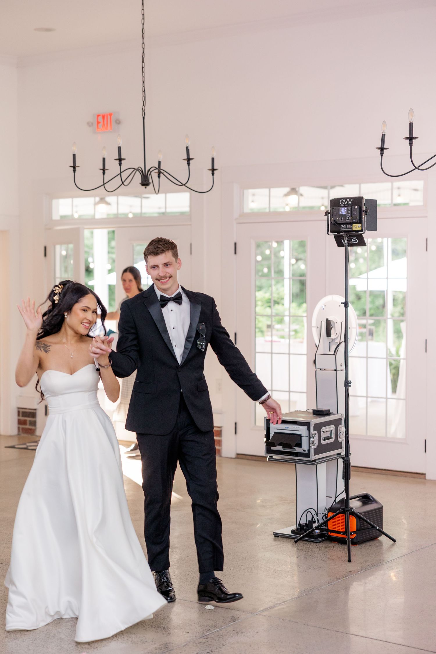 A couple dances in an elegant white reception room with chandelier and audio equipment.