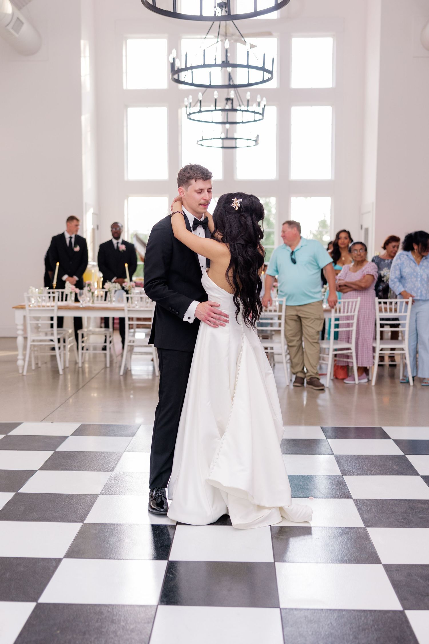 Newlyweds share first dance on elegant black and white checkered ballroom floor.