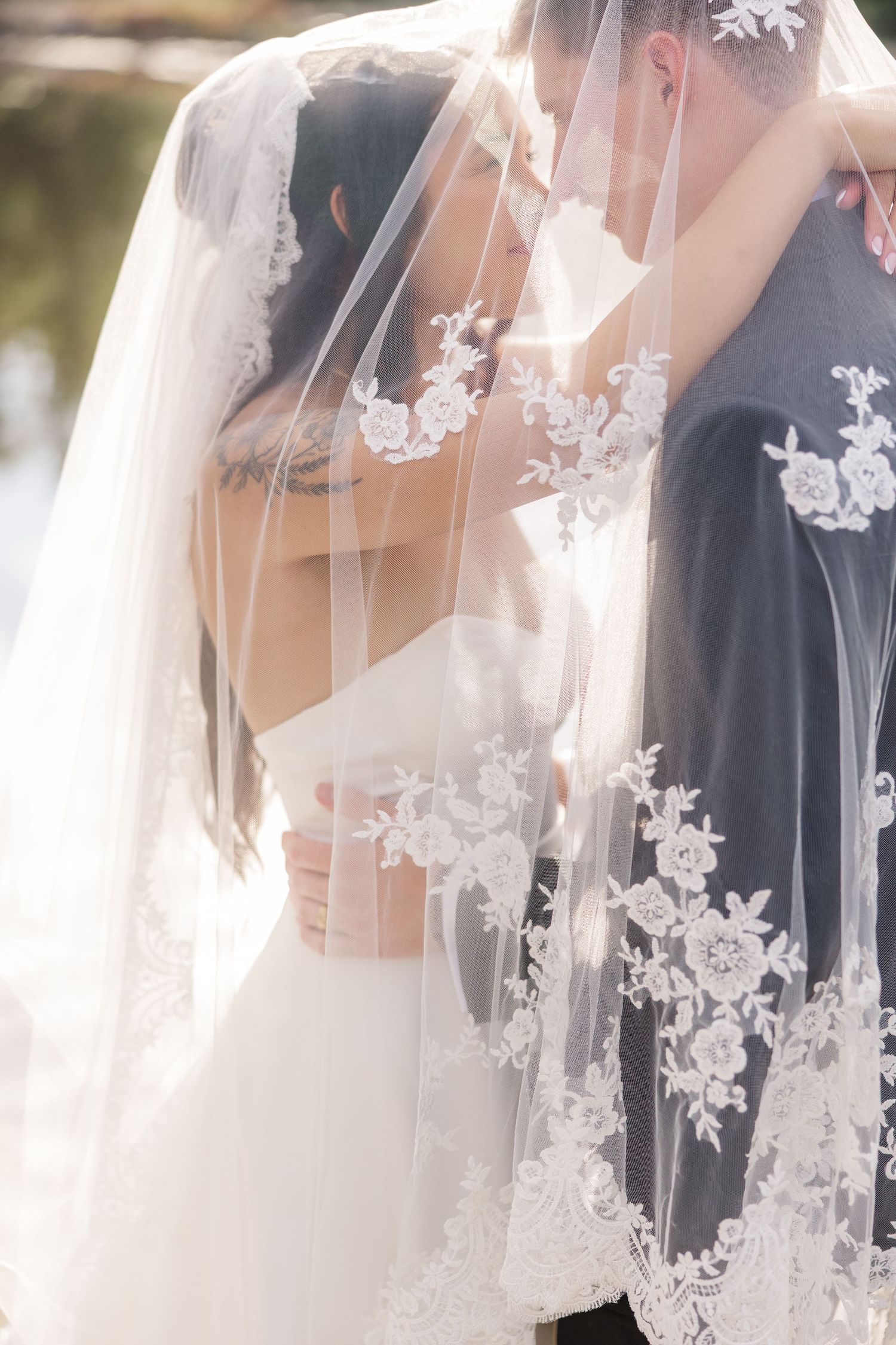 Close-up detail of ornate lace veil with floral appliques at outdoor wedding.