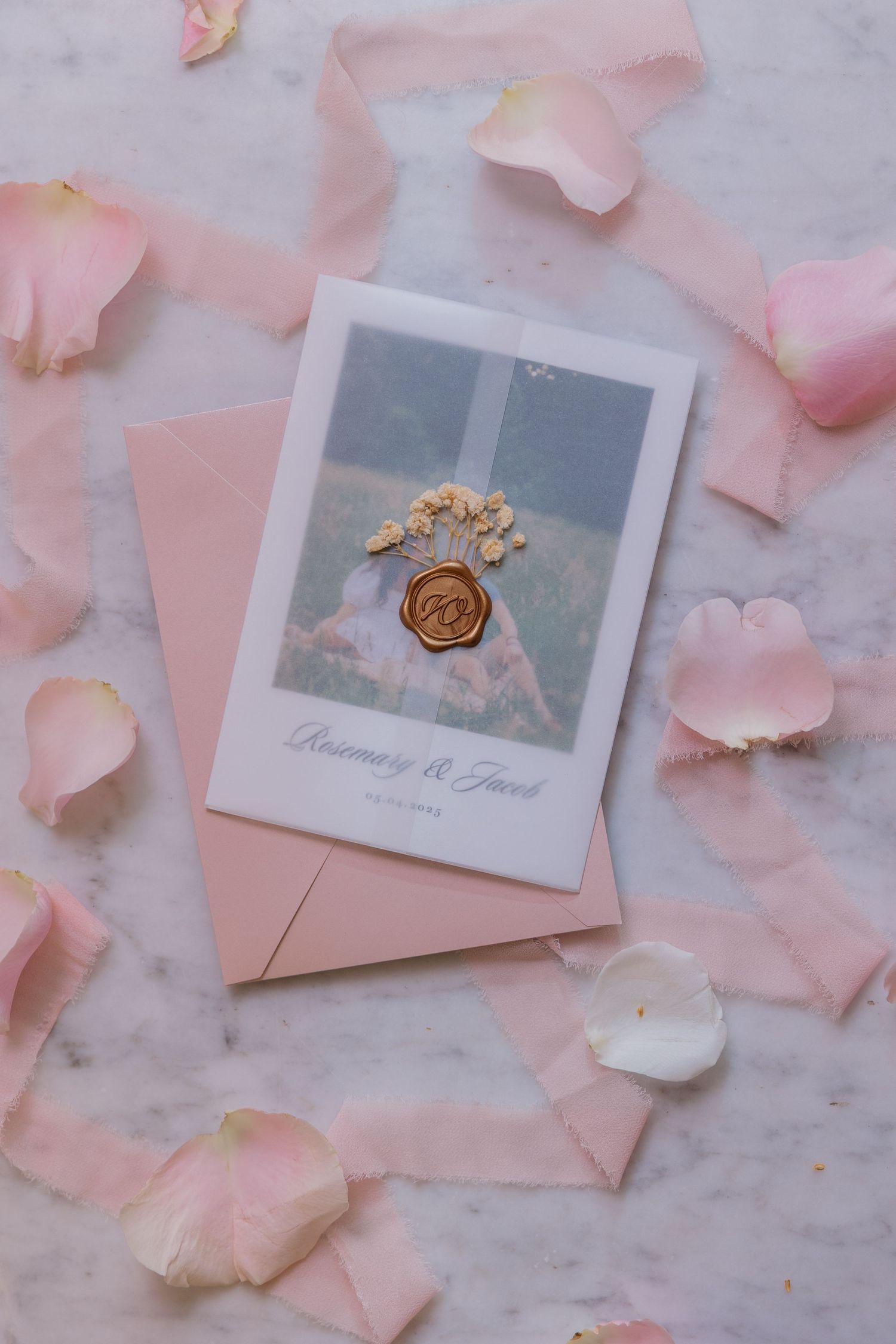 Wedding invitation with wax seal and pink rose petals on marble surface.