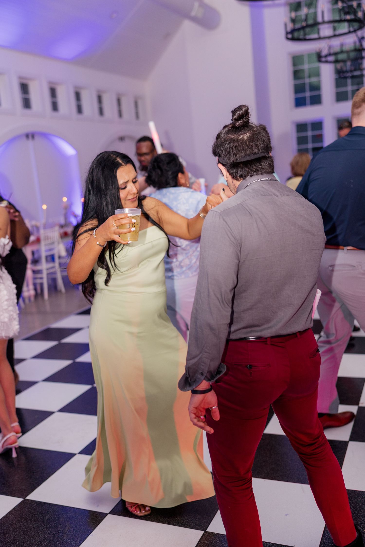 Guests dancing on a black and white checkered floor at an elegant reception with purple mood lighting.