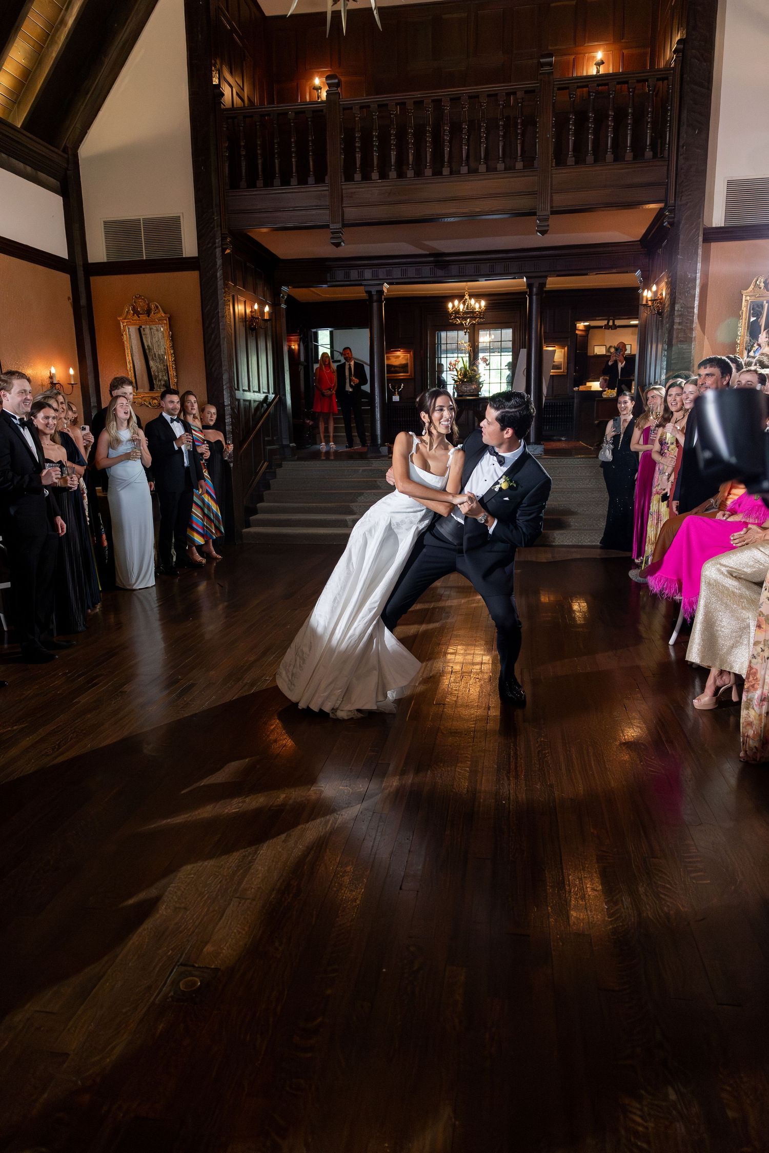 Bride and groom share their first dance in an elegant ballroom while wedding guests look on and applaud.