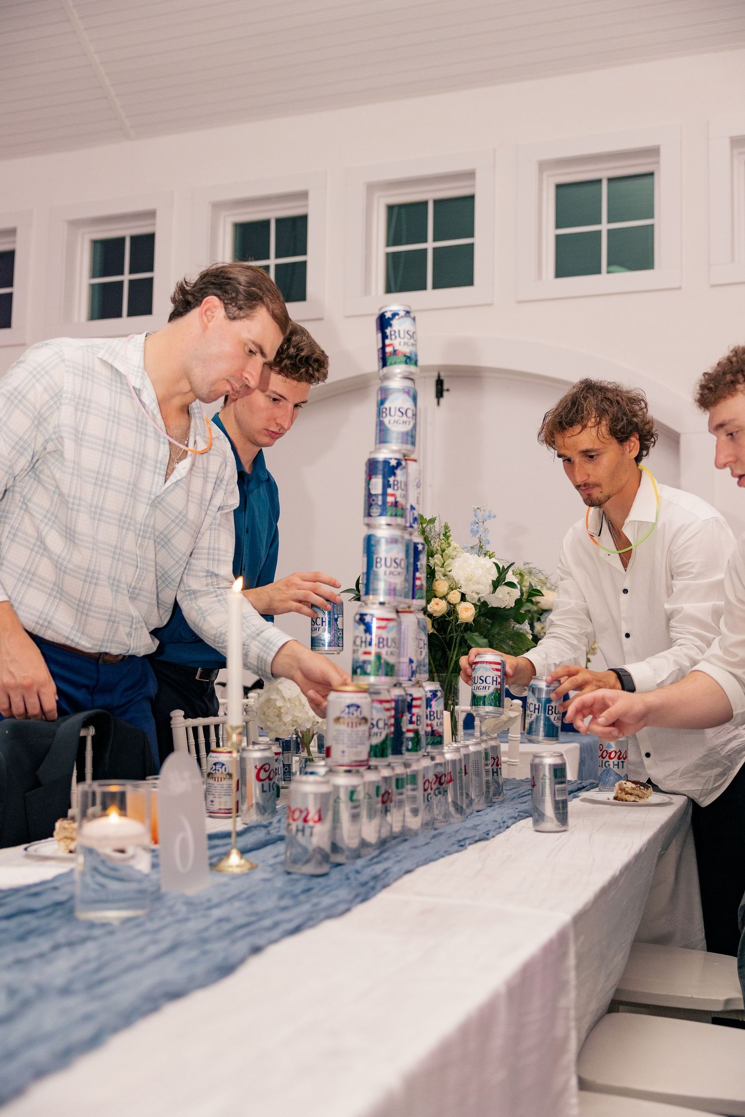 Groomsmen building a tower of beer cans on a decorated wedding reception table.