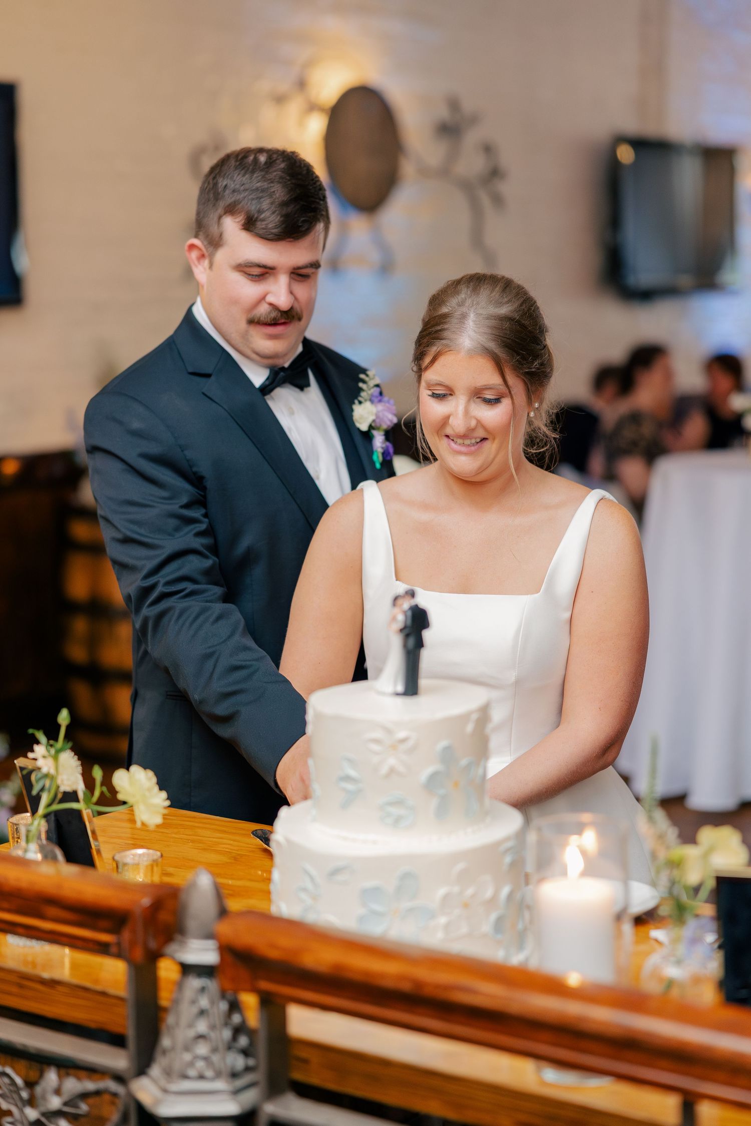 Bride and groom cut their two-tier white wedding cake decorated with blue floral details at reception.