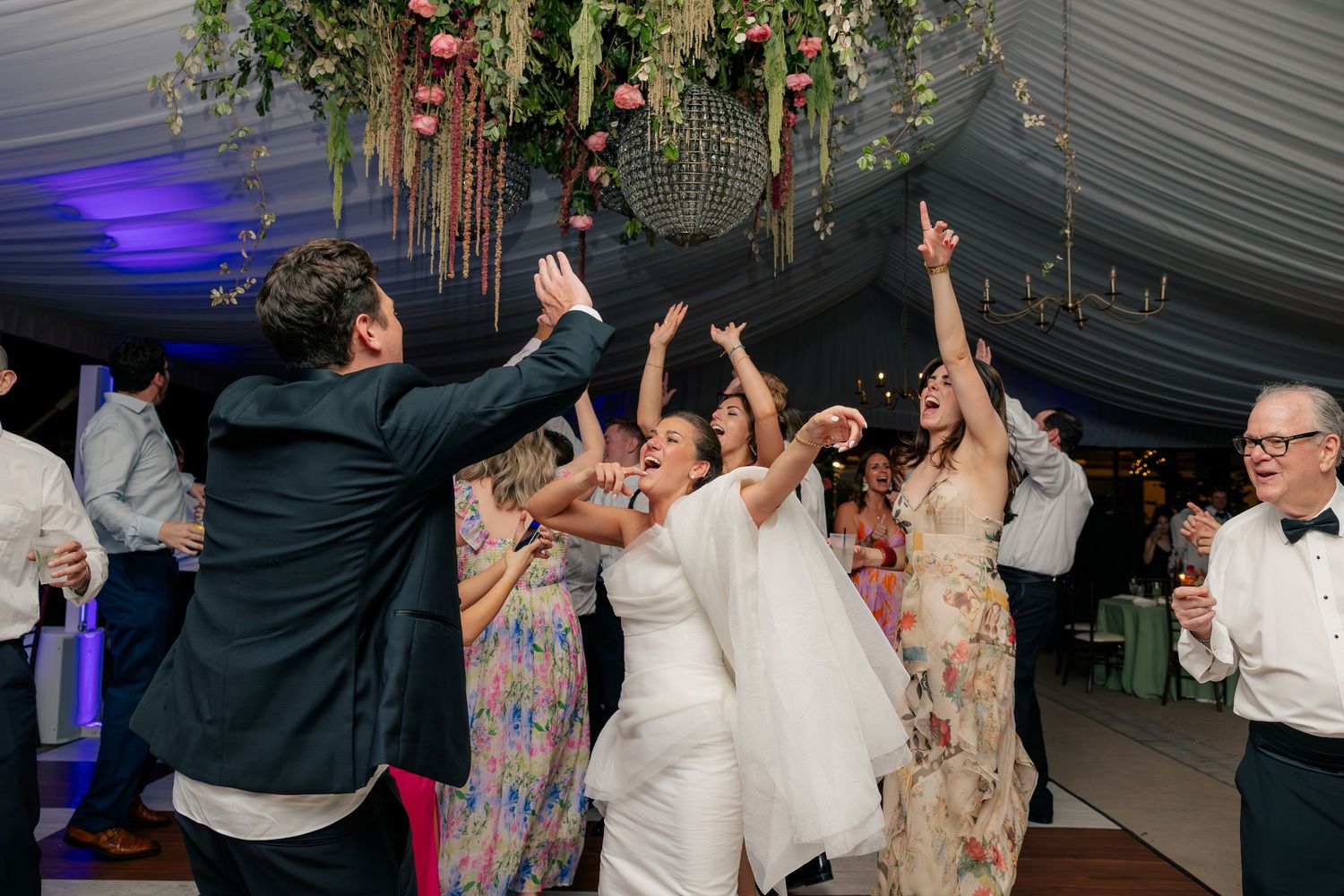 Bride and guests dancing joyfully under a disco ball at a lively wedding reception celebration.