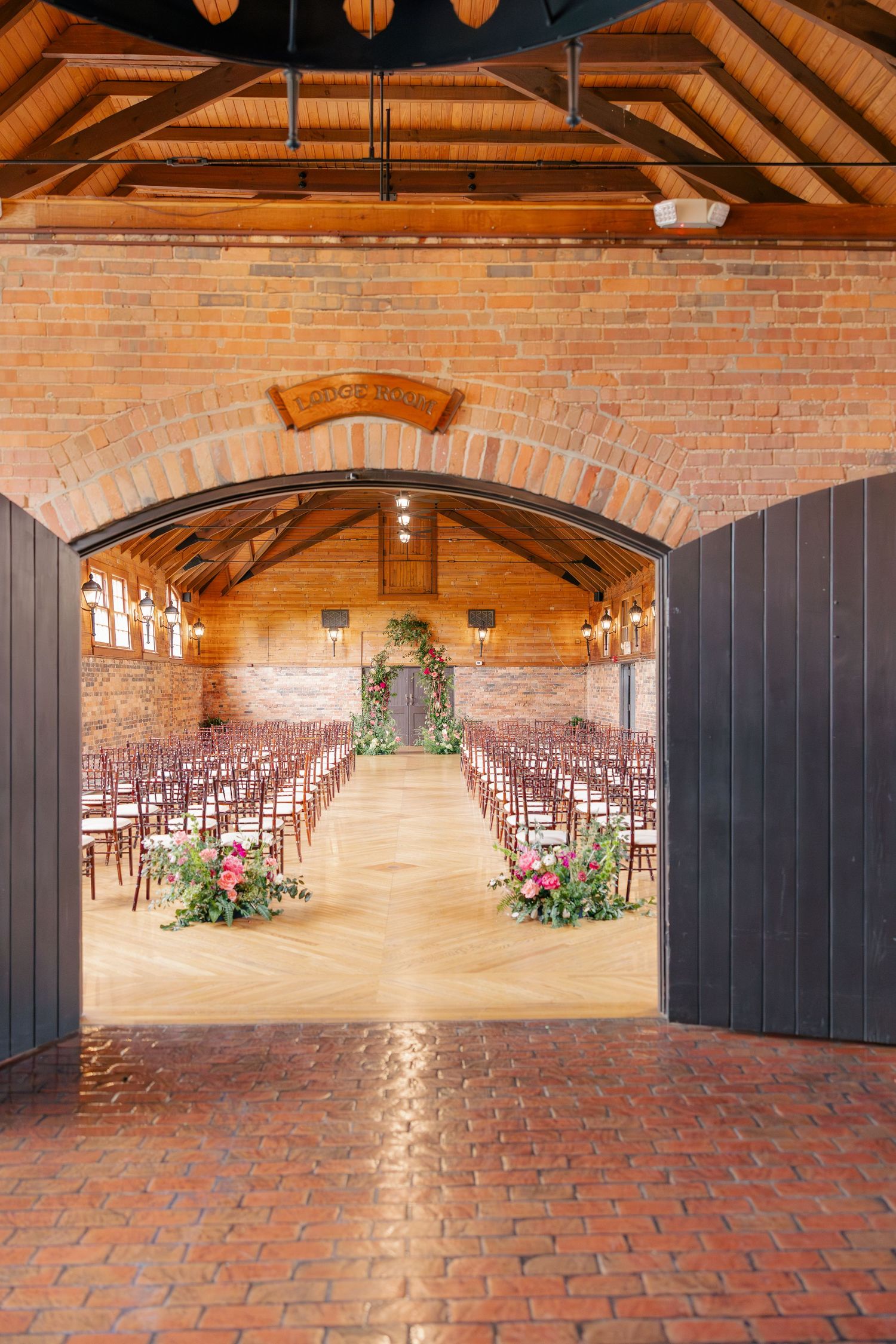 Rustic brick wedding ceremony venue with wooden arched ceiling, rows of chairs, and floral aisle.