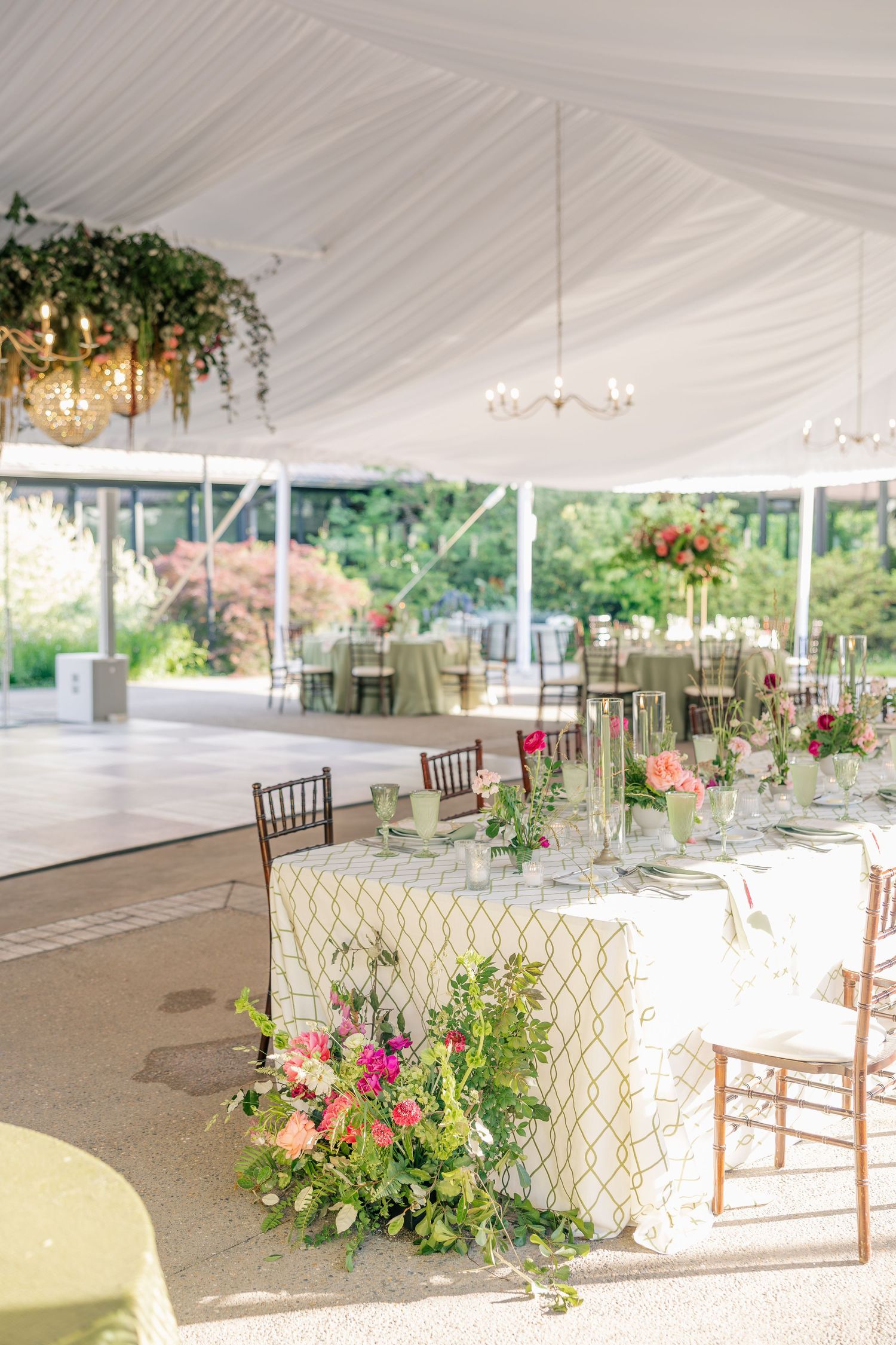 Elegant outdoor wedding reception under a white tent with floral centerpieces and garden views in the background.