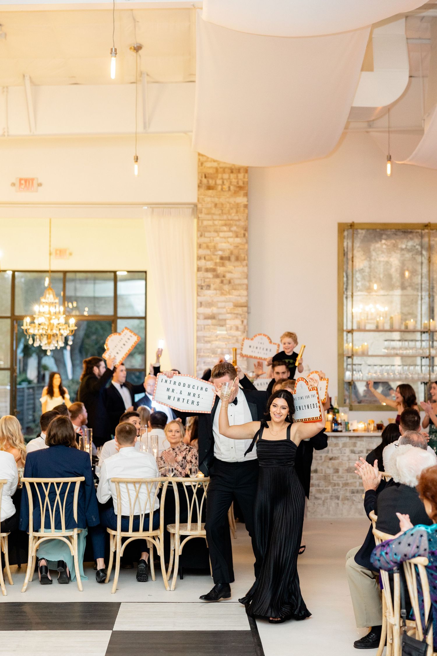 Wedding guests celebrate during a reception in an elegant venue with exposed brick walls and chandeliers.