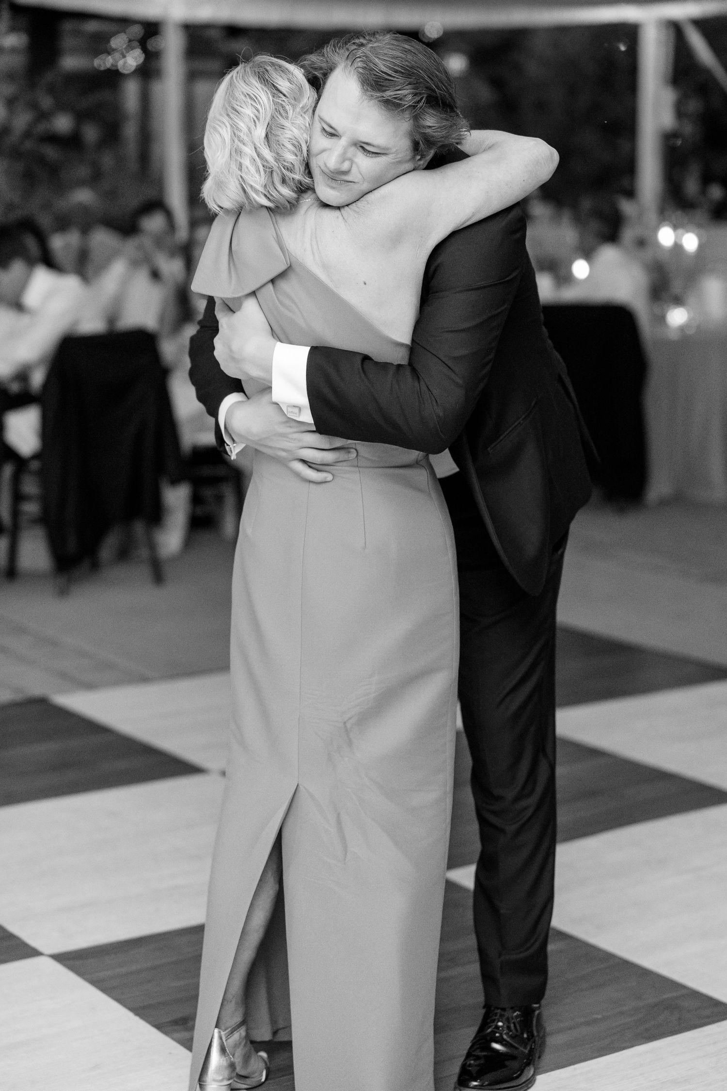 Groom and mother share an emotional embrace during mother-son dance on checkered floor at reception.