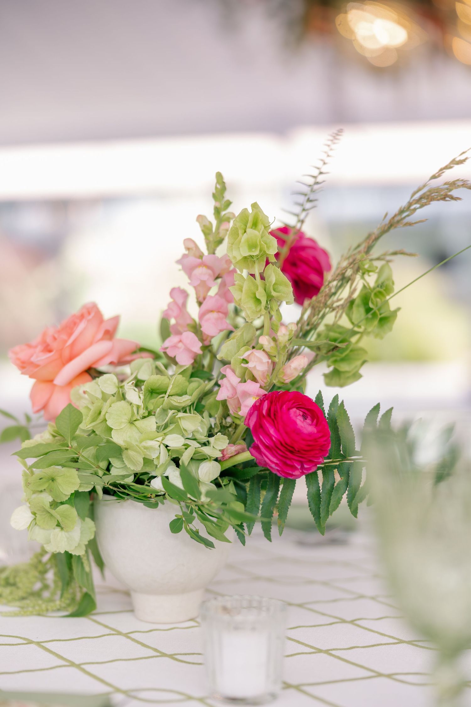 Elegant wedding centerpiece with pink ranunculus, coral roses, and green hydrangeas in white bowl.