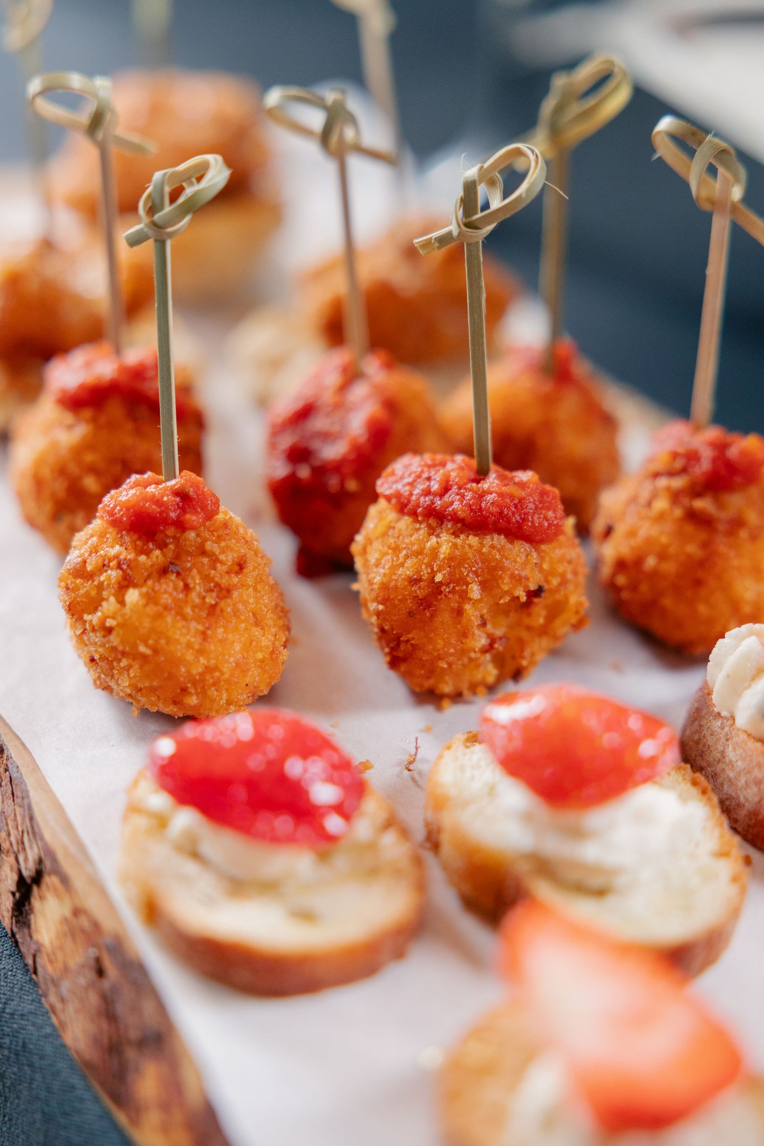 Assorted fried arancini and bruschetta wedding appetizers with tomato topping on rustic wooden board.