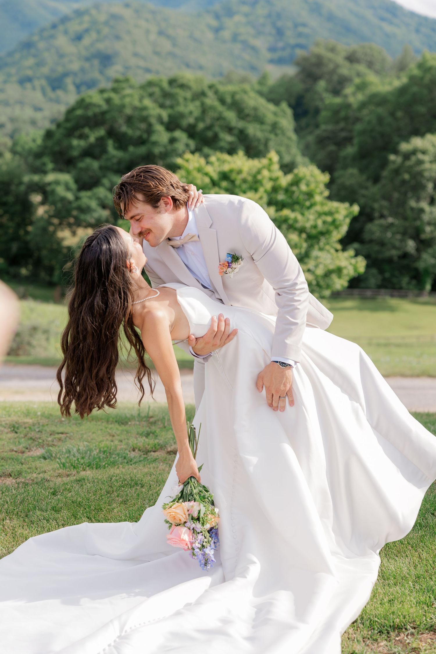 Romantic wedding couple dancing in a field with mountains in the background.