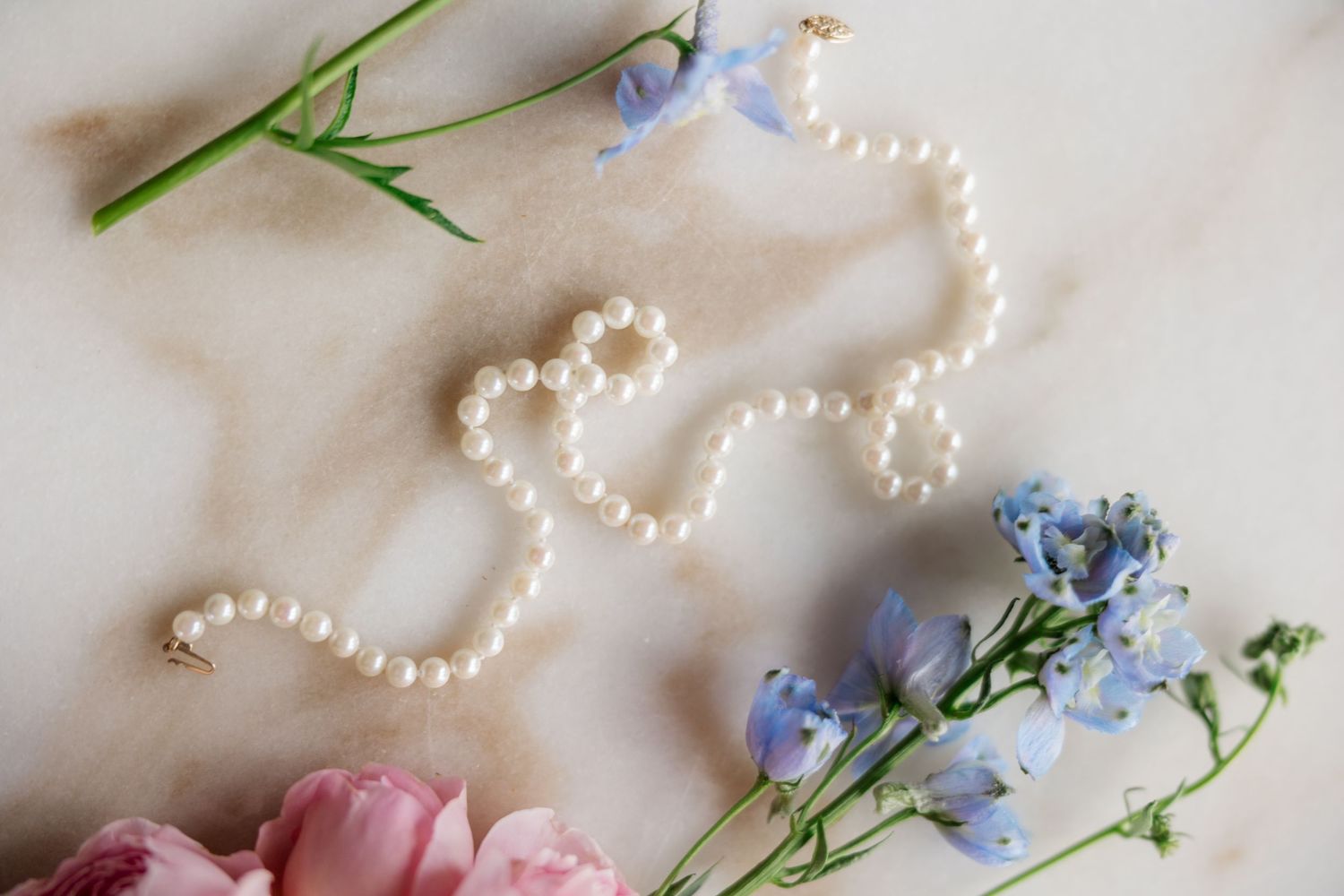 Delicate string of pearls arranged with pink tulips and blue wildflowers on a light fabric background.